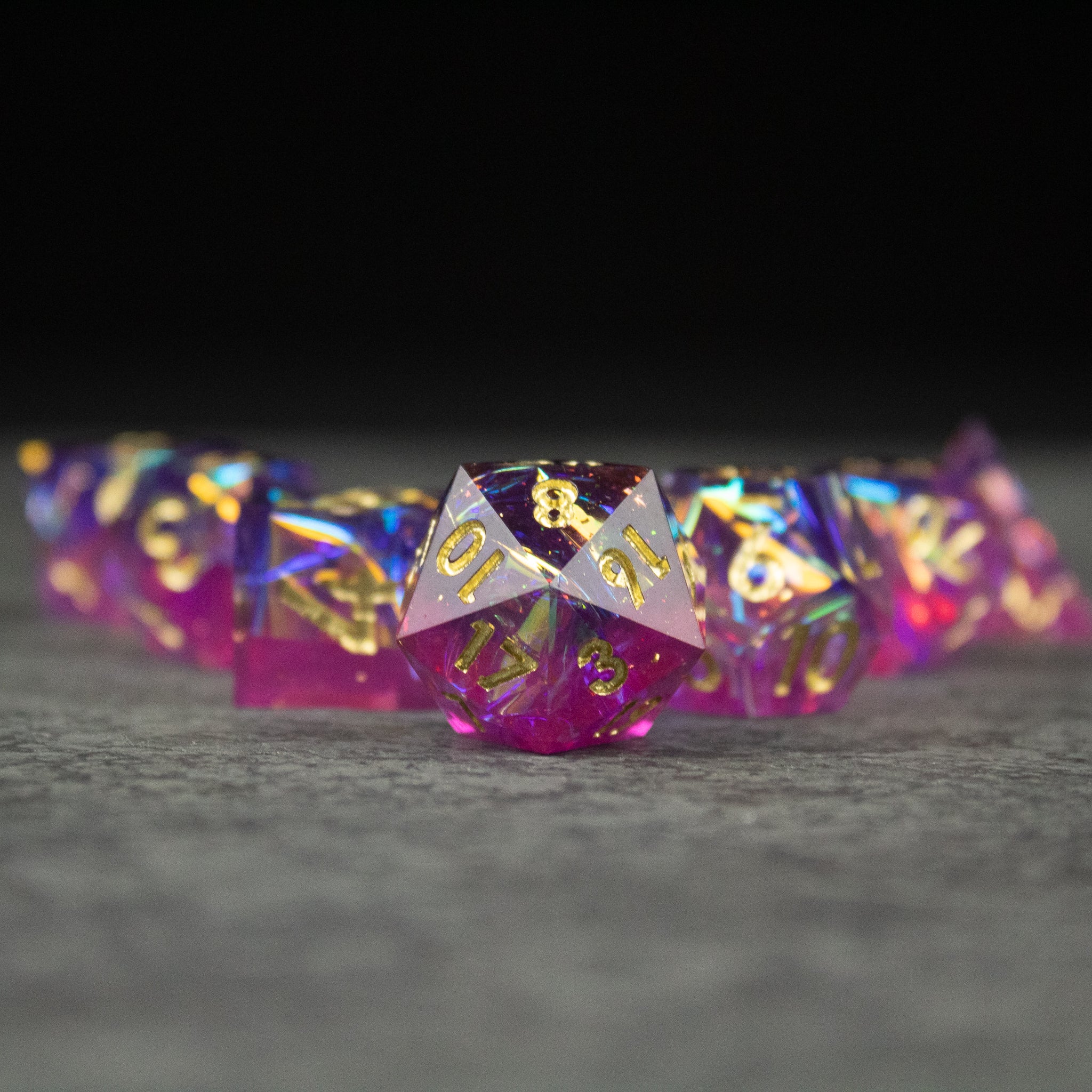 Aether Dice Set - Set of translucent pink and purple sharp-edged polyhedral dice with gold numbering on gray surface.