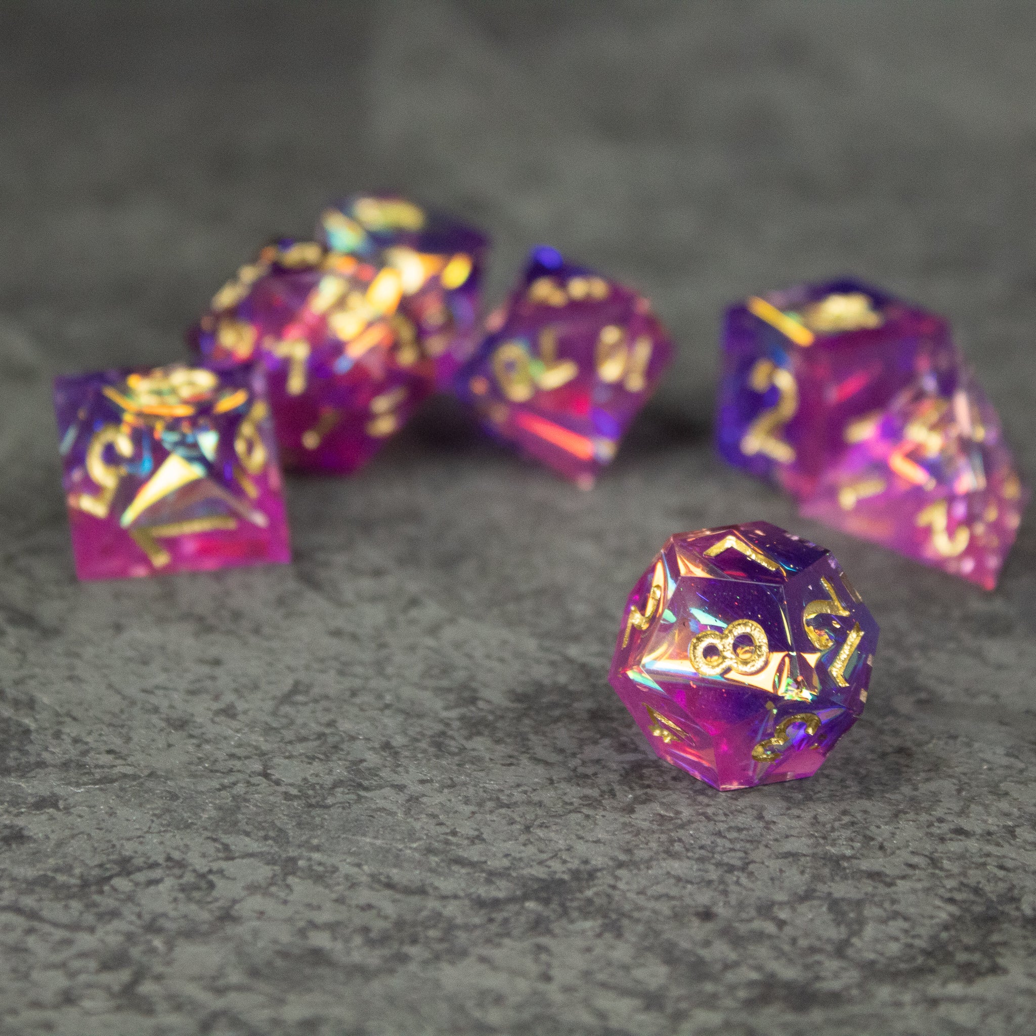 Aether Dice Set - Purple and pink sharp-edged polyhedral dice with gold numbering on gray surface.