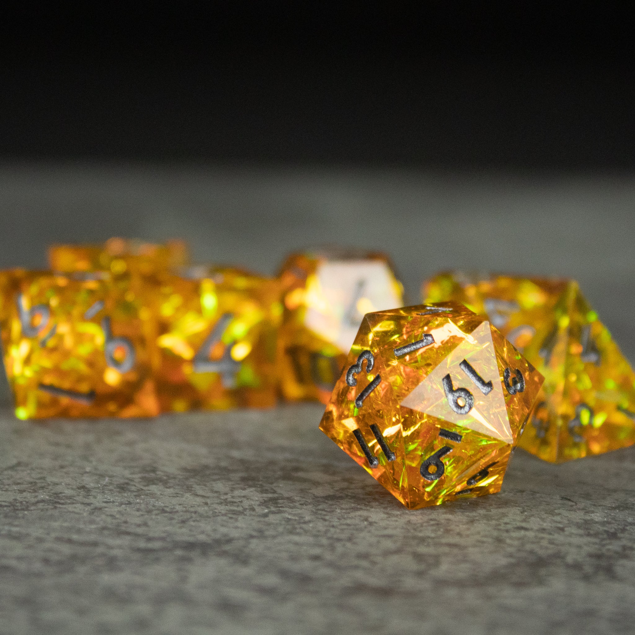 Golden Order Dice Set - Transparent gold twenty-sided dice with sharp edges and black numbering on a textured gray surface.