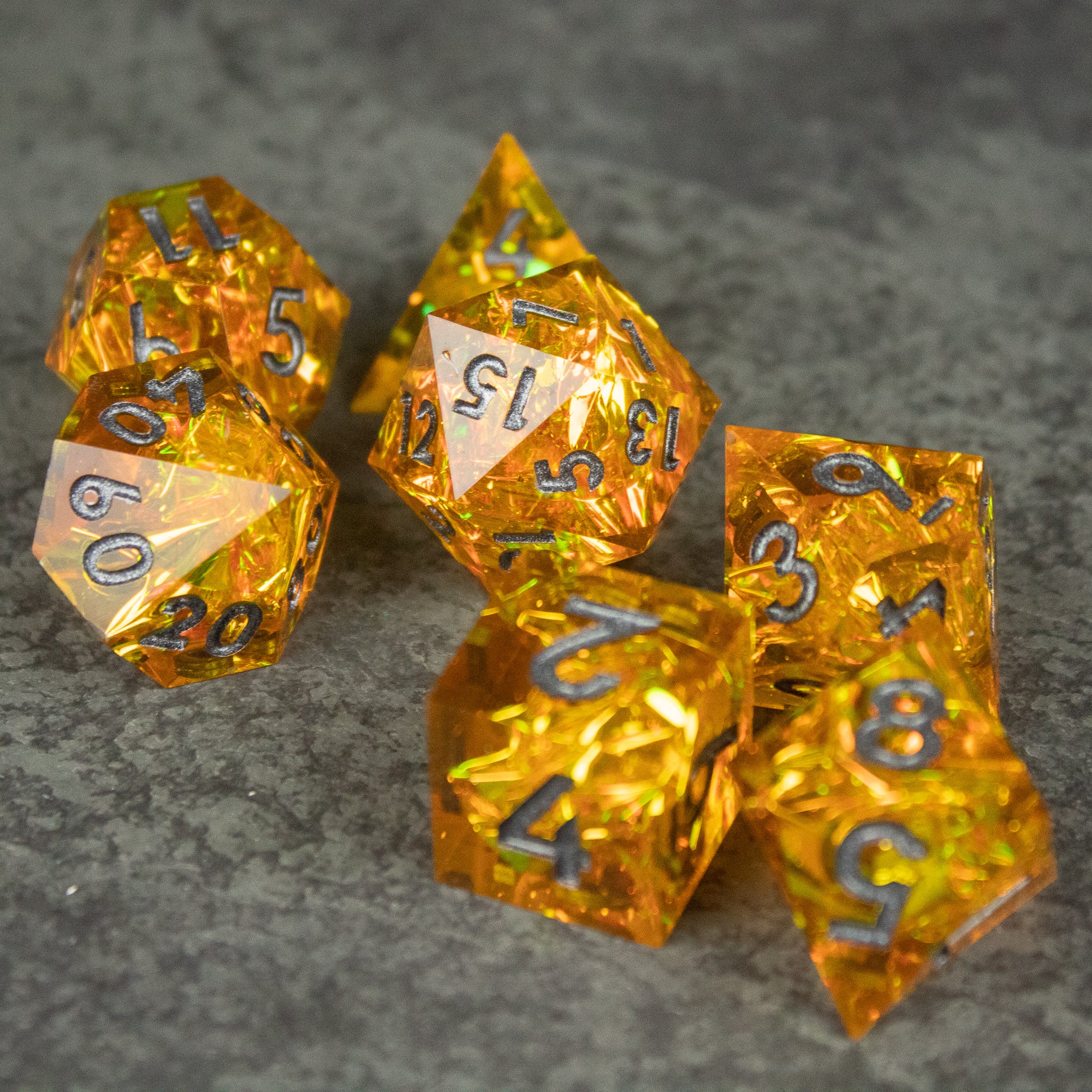 Golden Order Dice Set - Set of seven translucent golden polyhedral dice with sharp edges and metallic numbers on a gray surface.