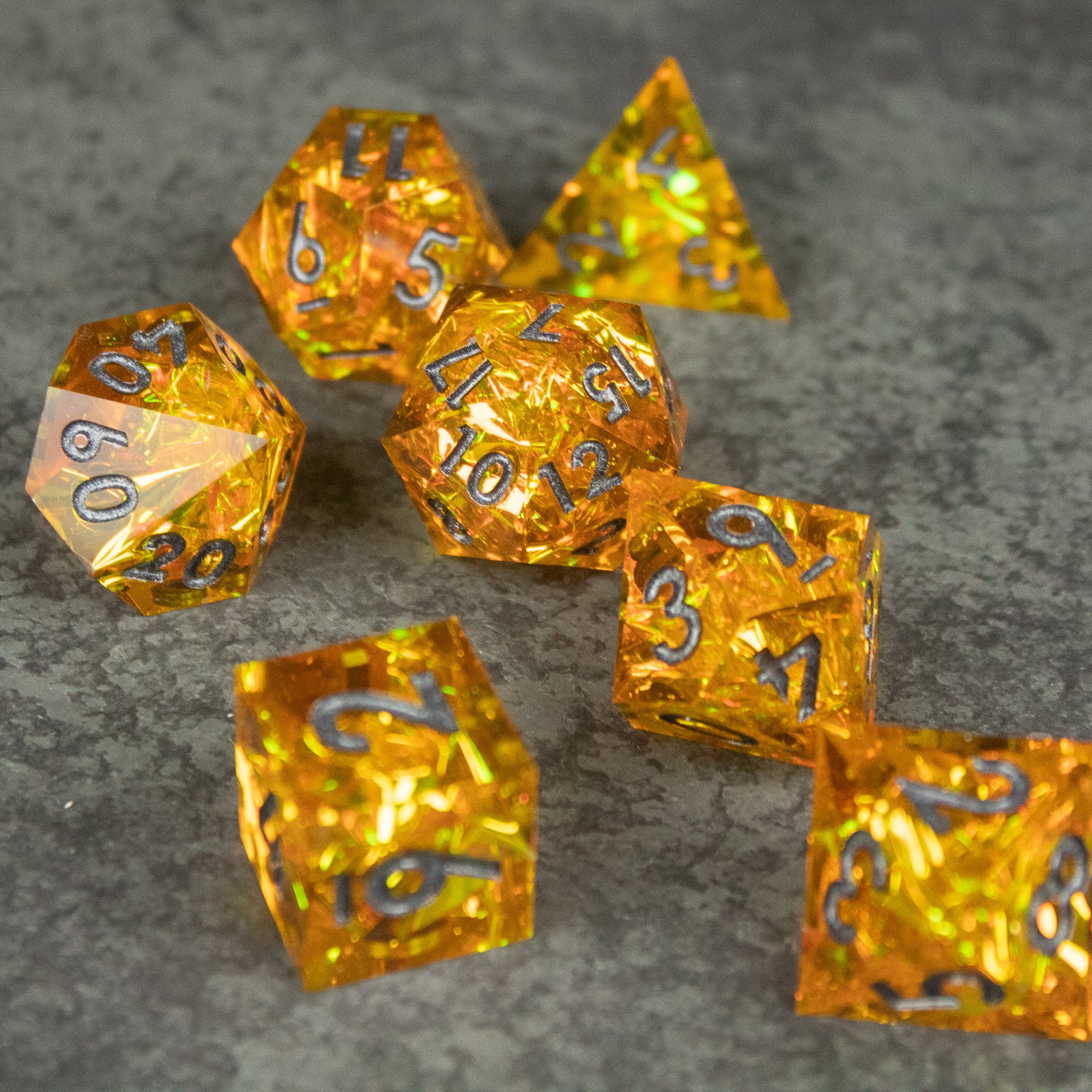 Golden Order Dice Set - Seven translucent golden polyhedral dice with sharp edges and white numbering on a gray textured surface.