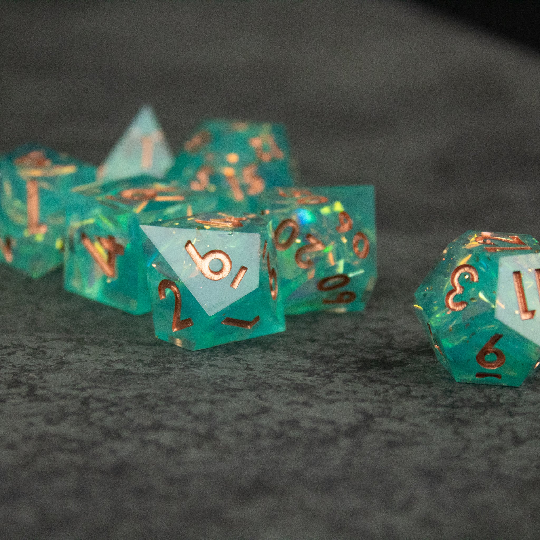 Residuum Dice Set - Translucent aquamarine polyhedral dice set with sharp edges and copper-colored numbers.