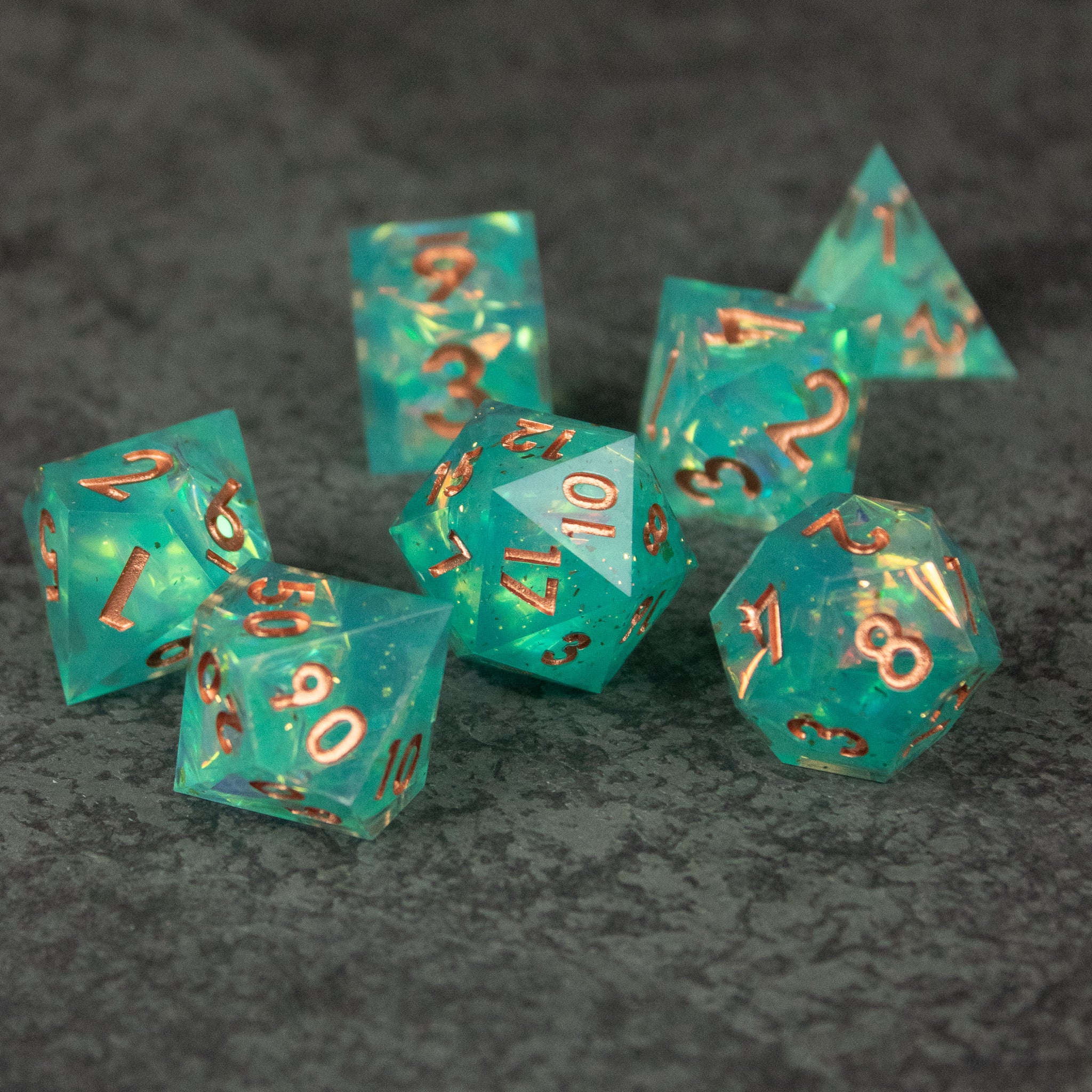 Residuum Dice Set - Set of seven translucent aquamarine polyhedral dice with sharp edges and copper-colored numbers.