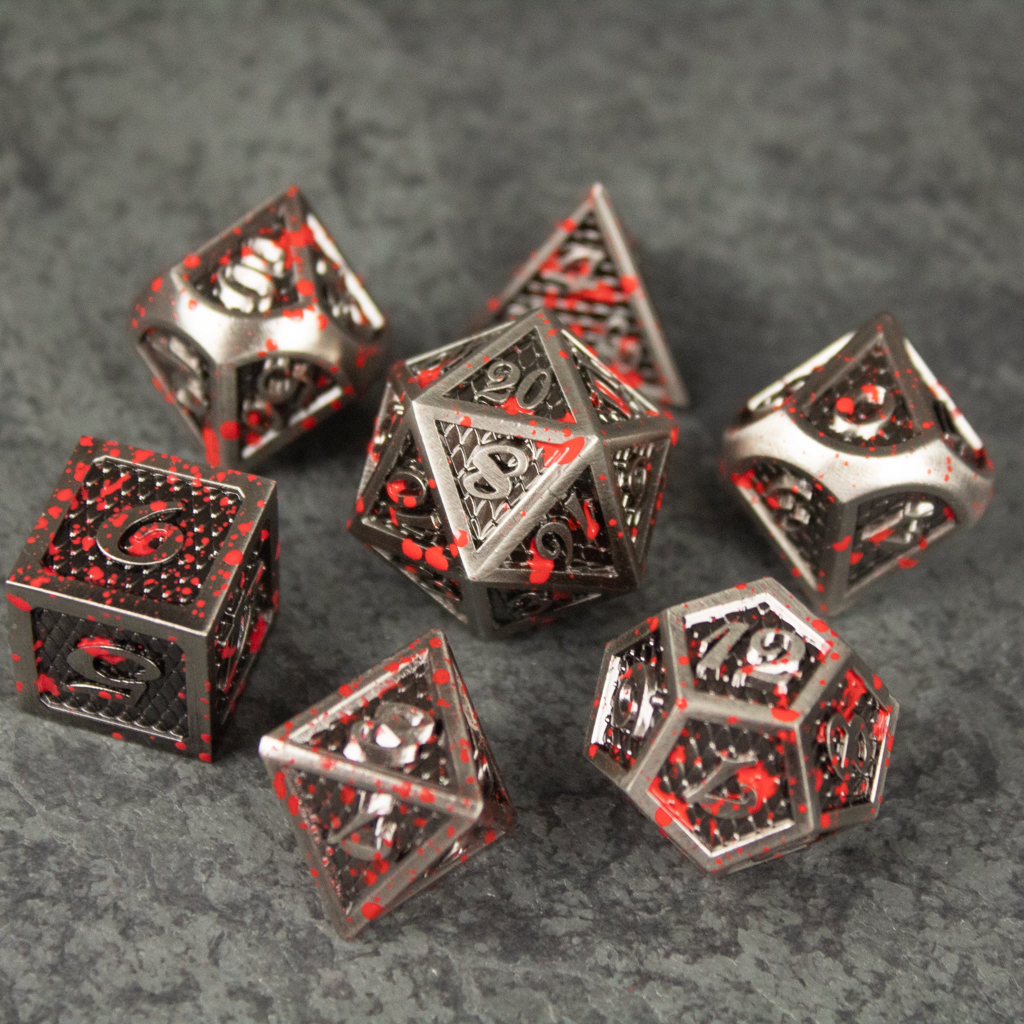 Marauder Dice Set - Set of seven metallic red and silver polyhedral dice with intricate engraved designs on a gray stone surface.