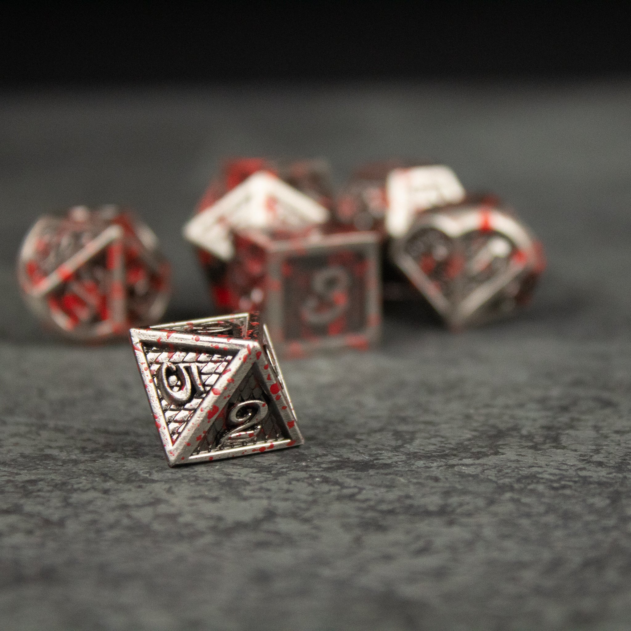 Marauder Dice Set - Silver metal d20 dice with intricate tribal engravings and red enamel details on black background.