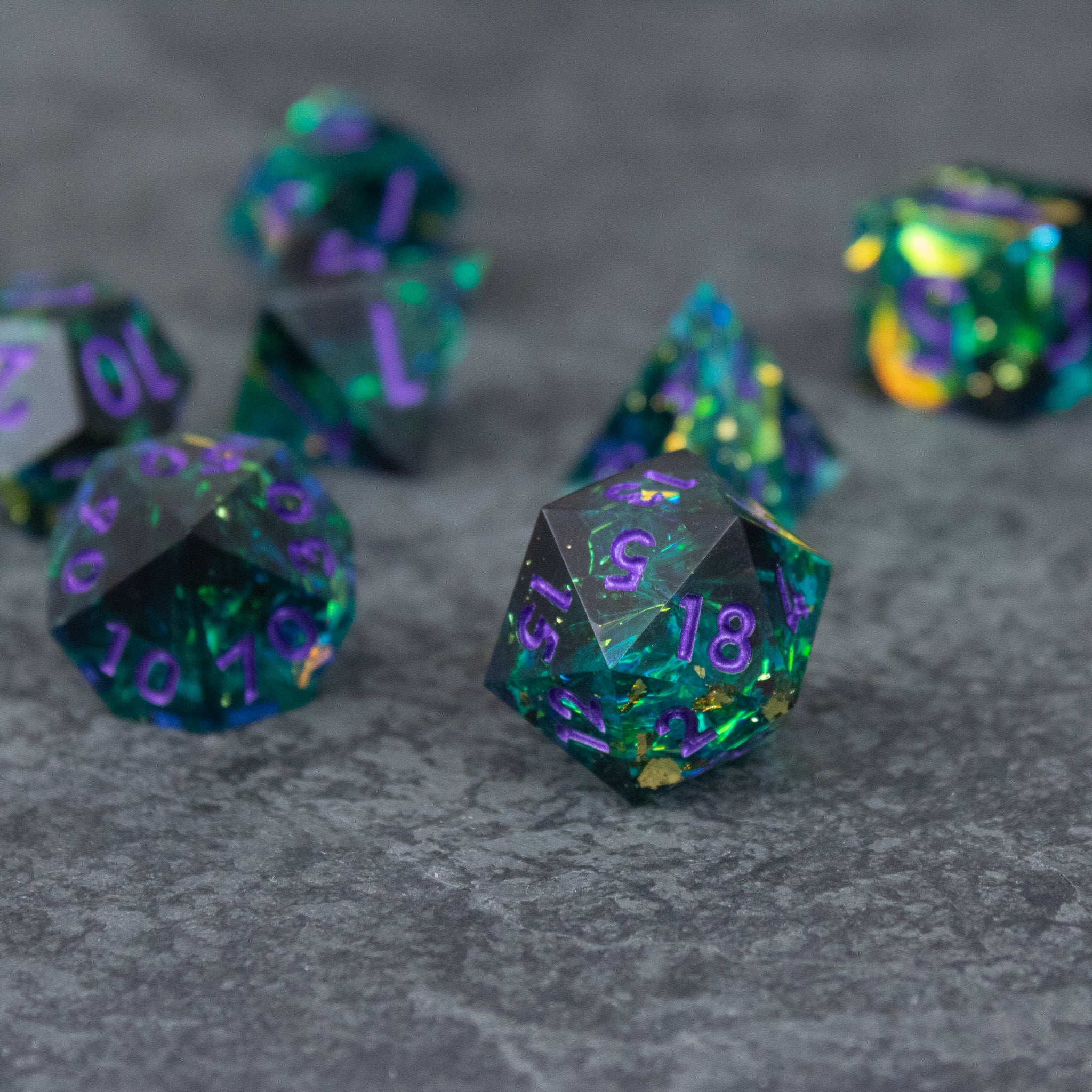 Deathblight Dice Set - Translucent blue-green polyhedral dice set with sharp edges and purple numbering on a gray surface.