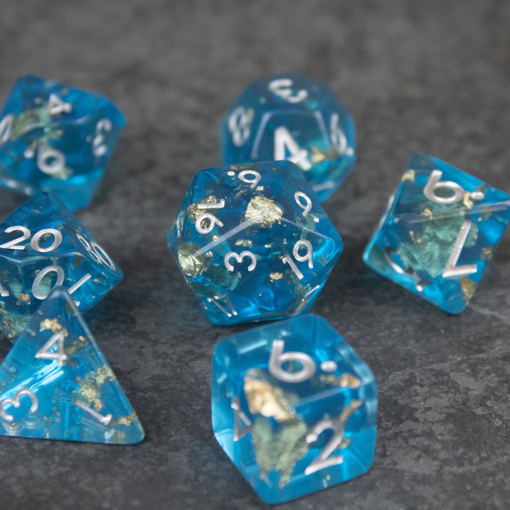 Blue Foil Dice Set - Transparent blue polyhedral dice set with silver foil flakes and white numbers on a dark gray surface.