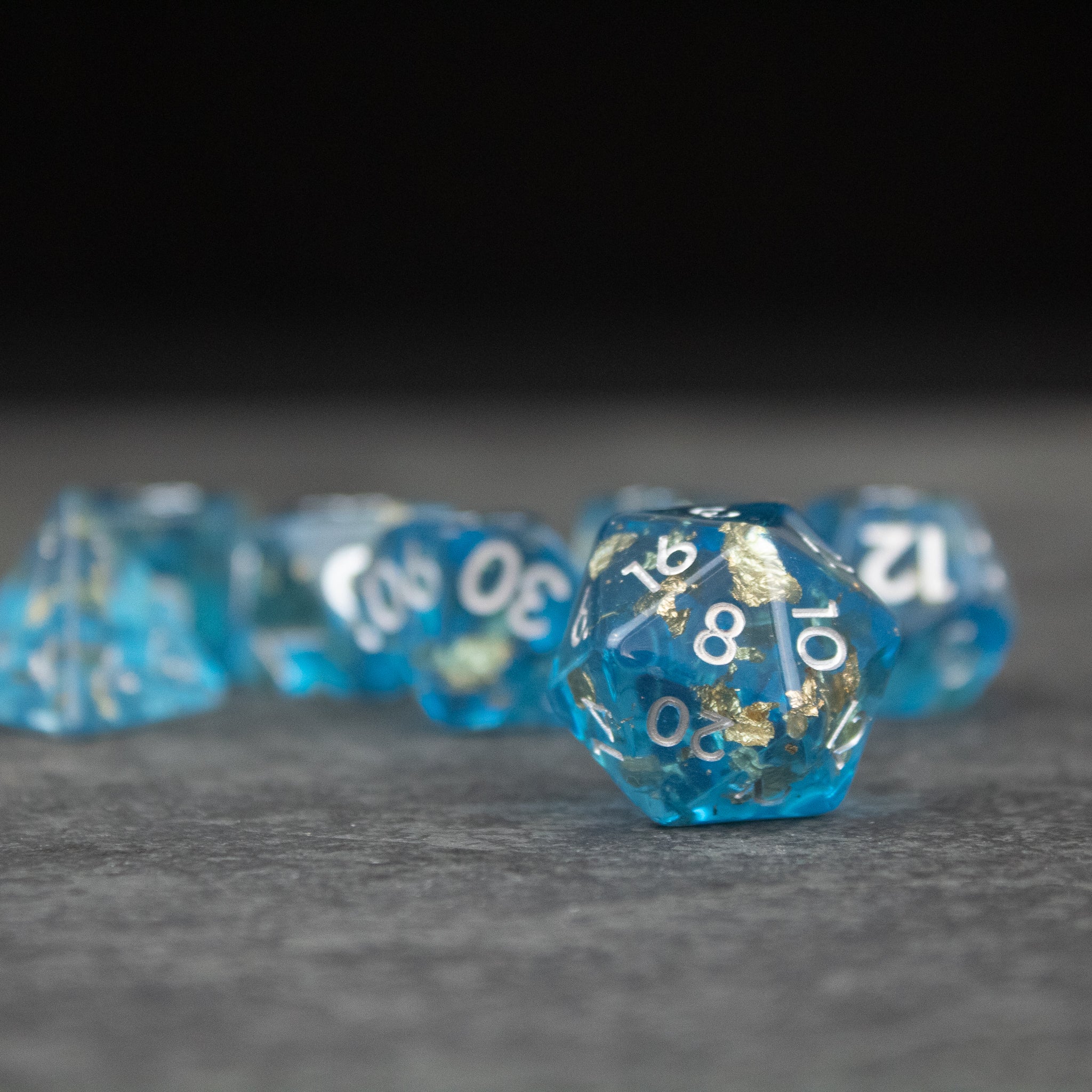 Blue Foil Dice Set - Translucent blue 20-sided dice with gold foil numbers, set on gray surface.