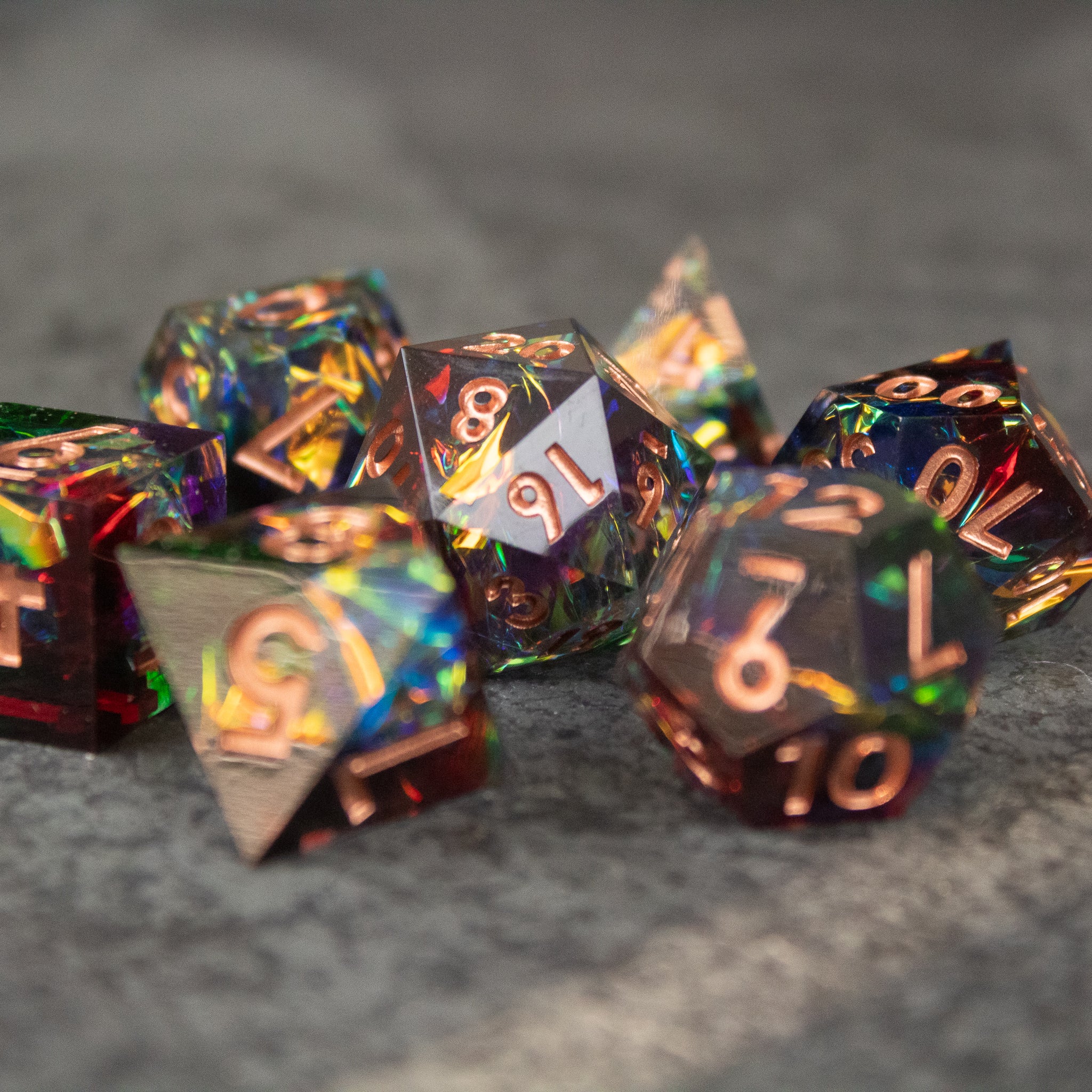 Aurora Dice Set - Sharp-edged rainbow polyhedral dice set with iridescent finish and gold numbering on gray surface.