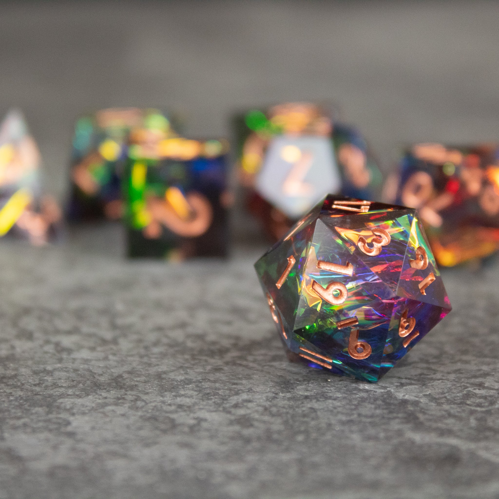 Aurora Dice Set - Transparent multicolored d20 dice with sharp edges and gold numbering on a gray surface.