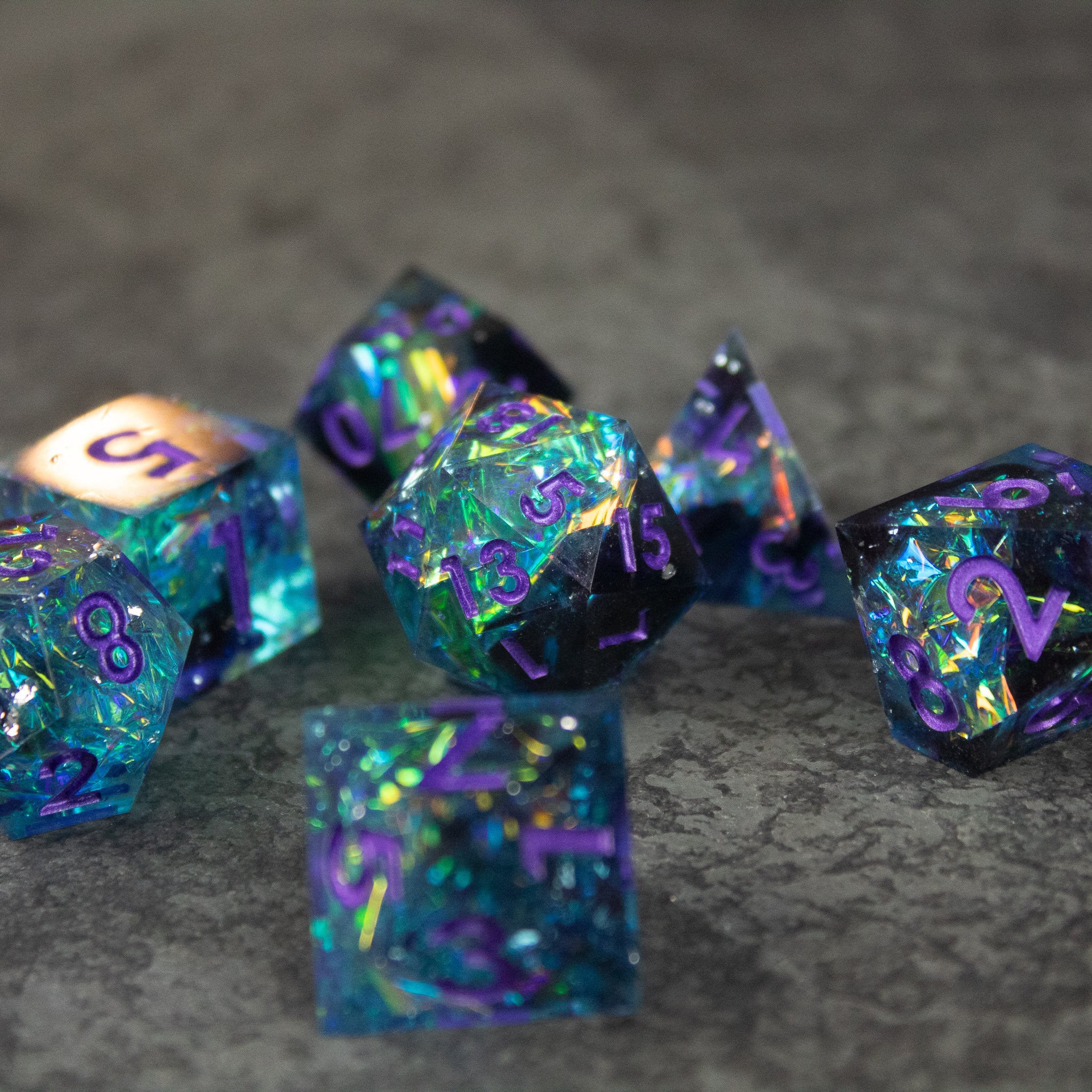 Frostbite Dice Set - Set of black and blue sharp-edged polyhedral dice with iridescent, frost-like patterns and purple numbers on a gray surface.