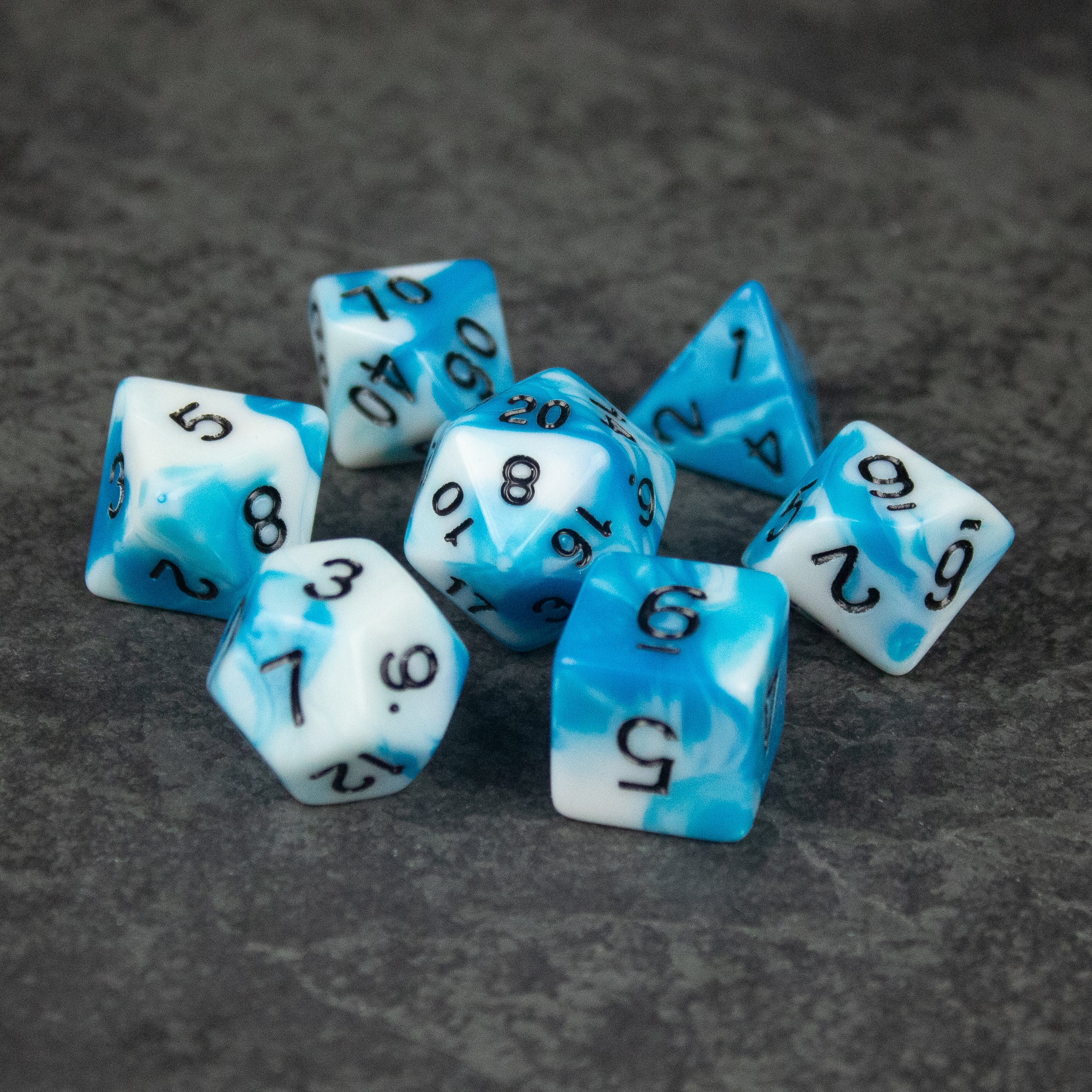 Blue and White Marbled Dice Set - Seven-piece blue and white marbled acrylic dice set with black numbering on dark textured surface.