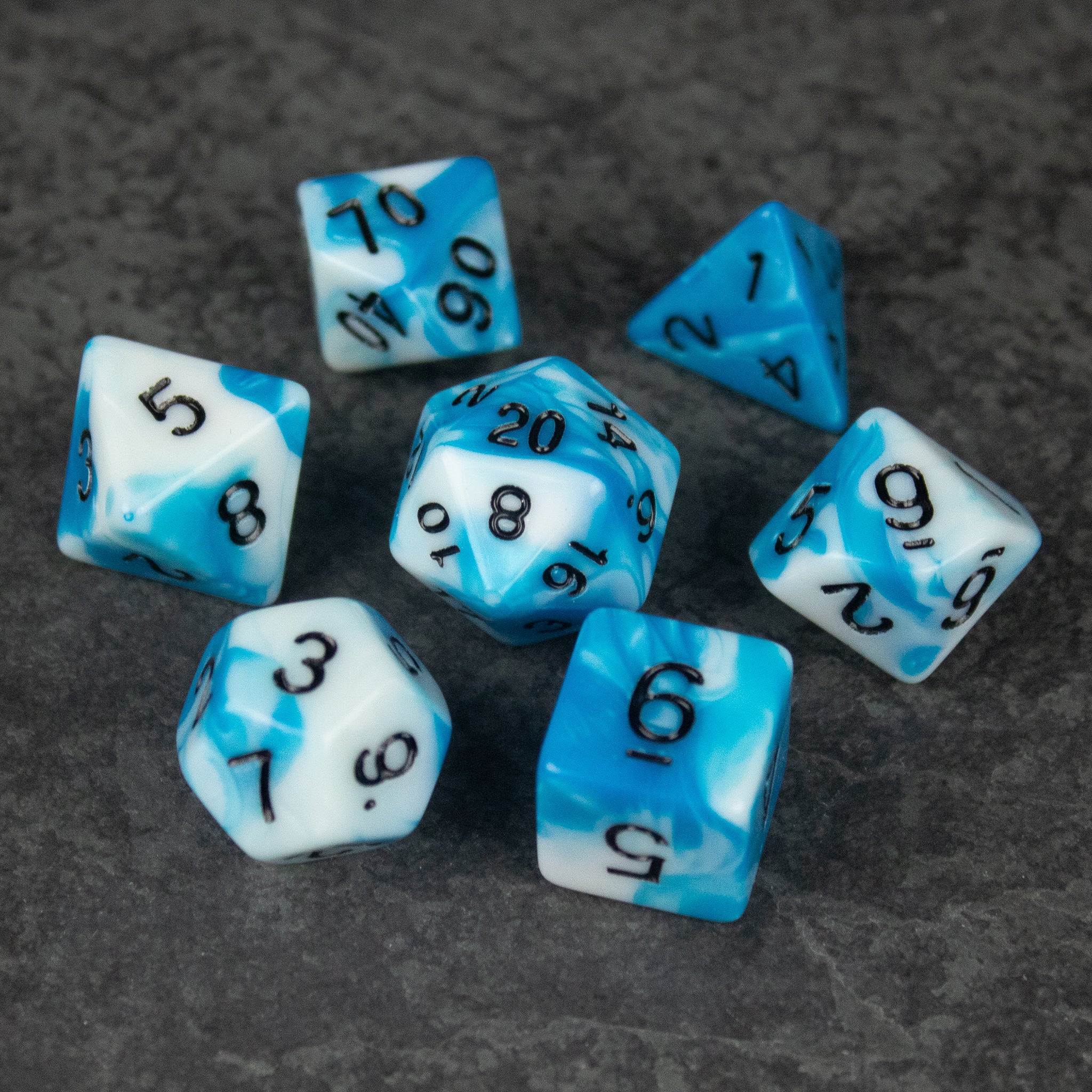 Blue and White Marbled Dice Set - Seven-piece blue and white marbled acrylic dice set with black numbering on dark surface.