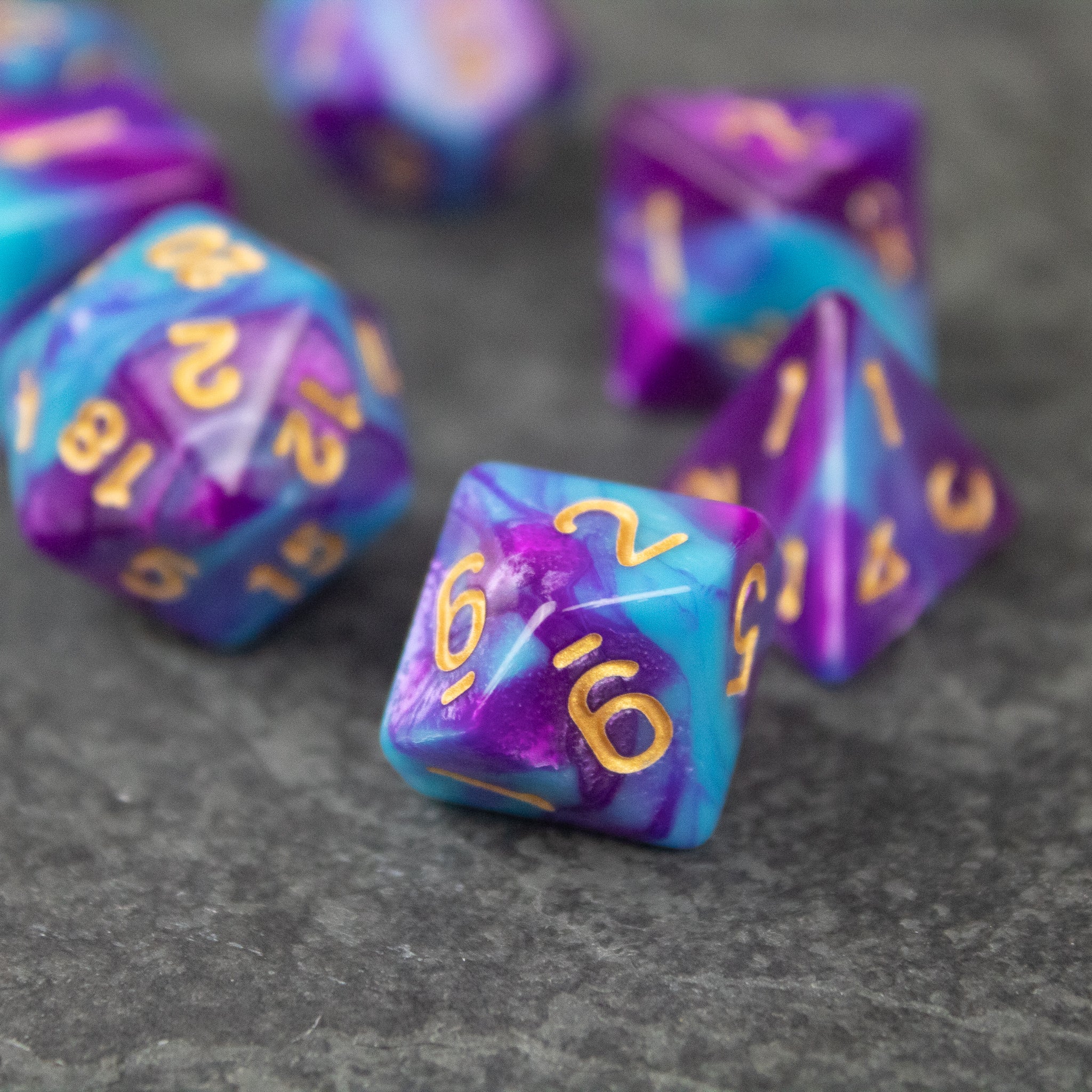 Purple and Blue Marbled Dice Set - Set of acrylic dice with a purple and blue marbled pattern and gold numbers on a gray surface.