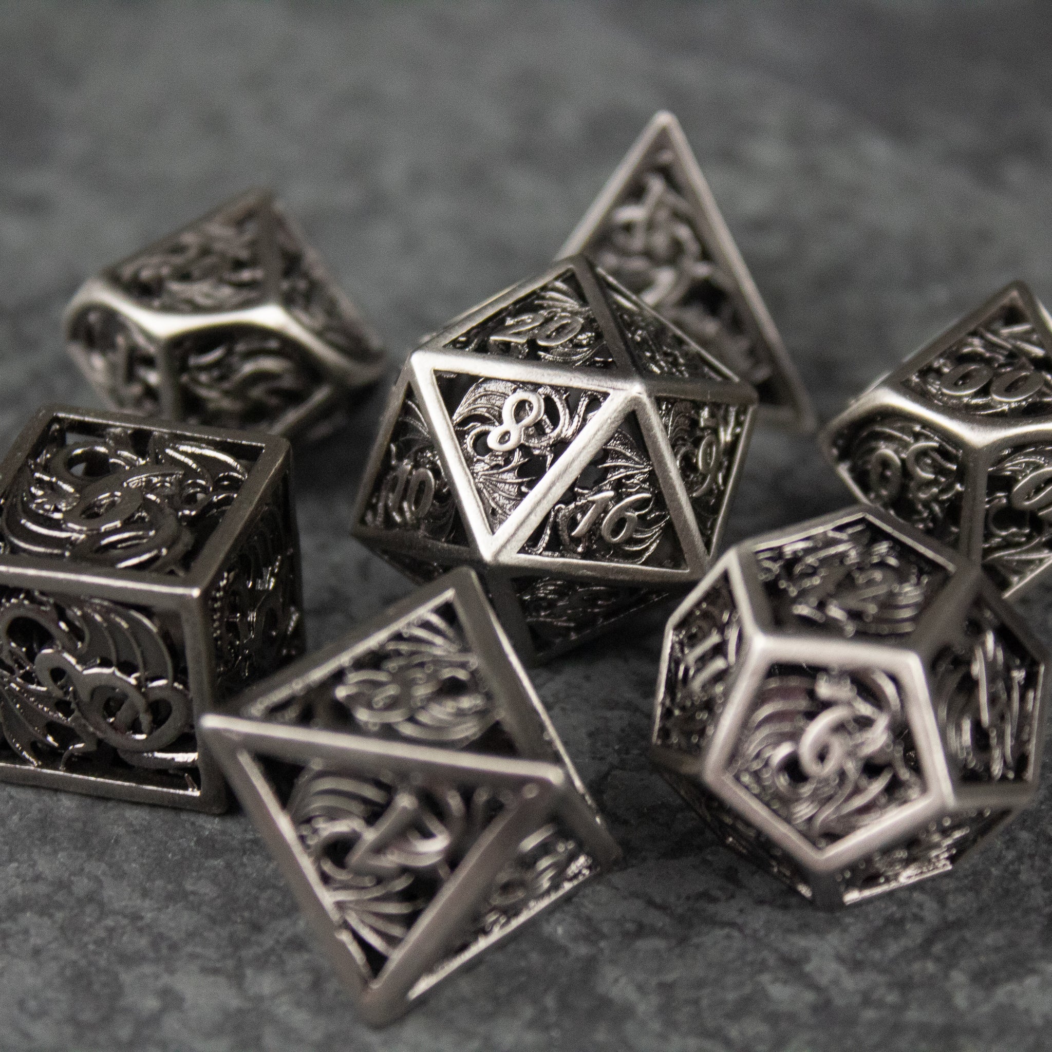 Dragon Cult Hollow Dice Set - Set of seven hollow metal dice with intricate dragon-themed filigree designs on each face.