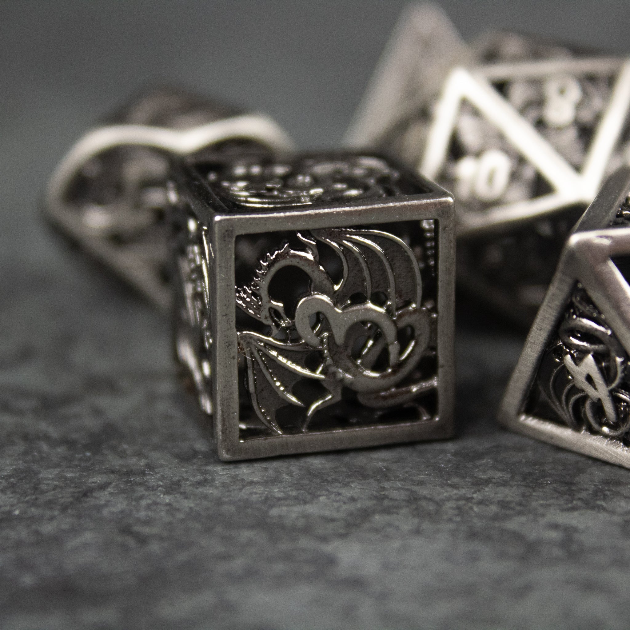 Dragon Cult Hollow Dice Set - Metal hollow dice set with intricate dragon cutout designs and a dark silver finish.