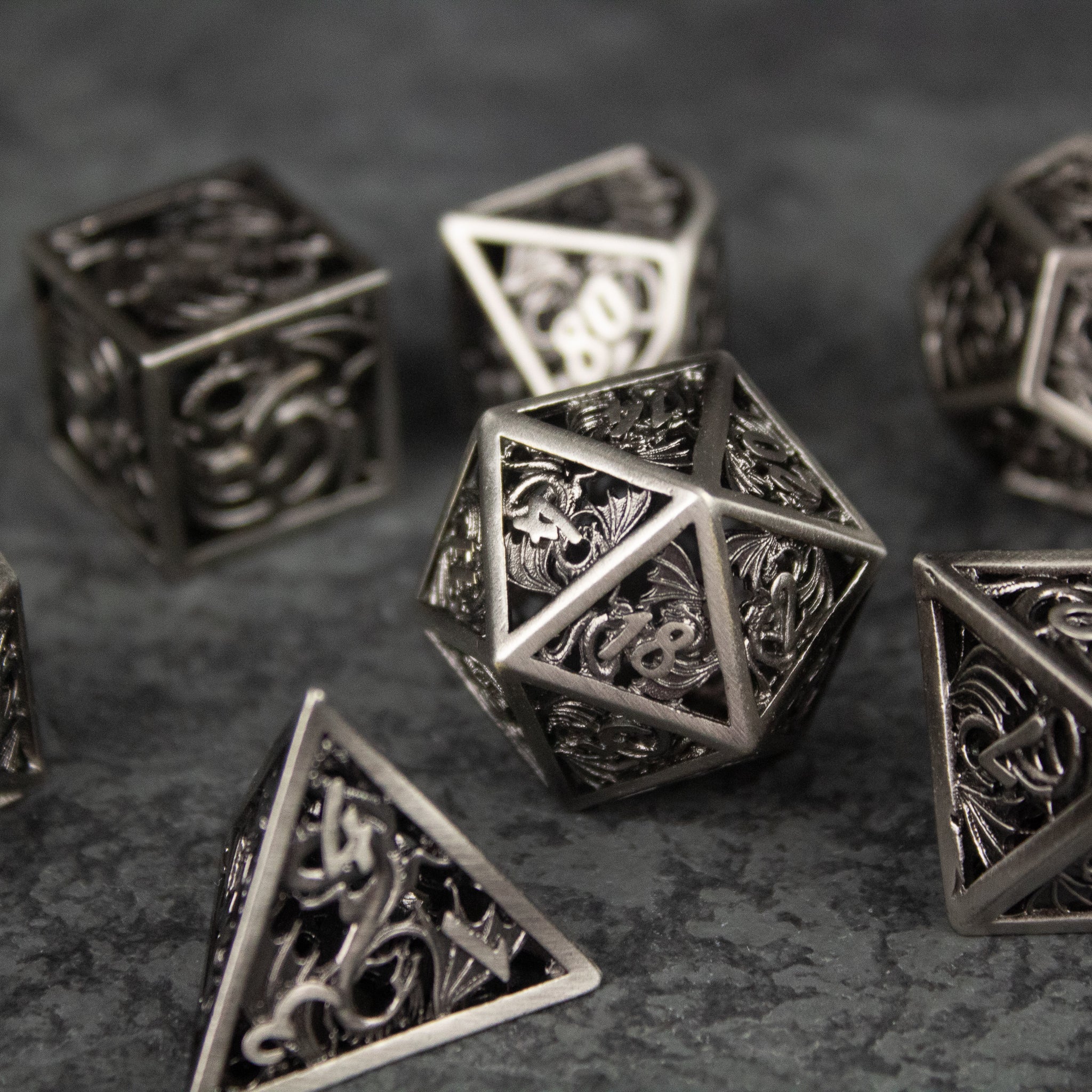 Dragon Cult Hollow Dice Set - Silver metal hollow dice set with intricate dragon designs on each face, including a 20-sided die and other polyhedral.