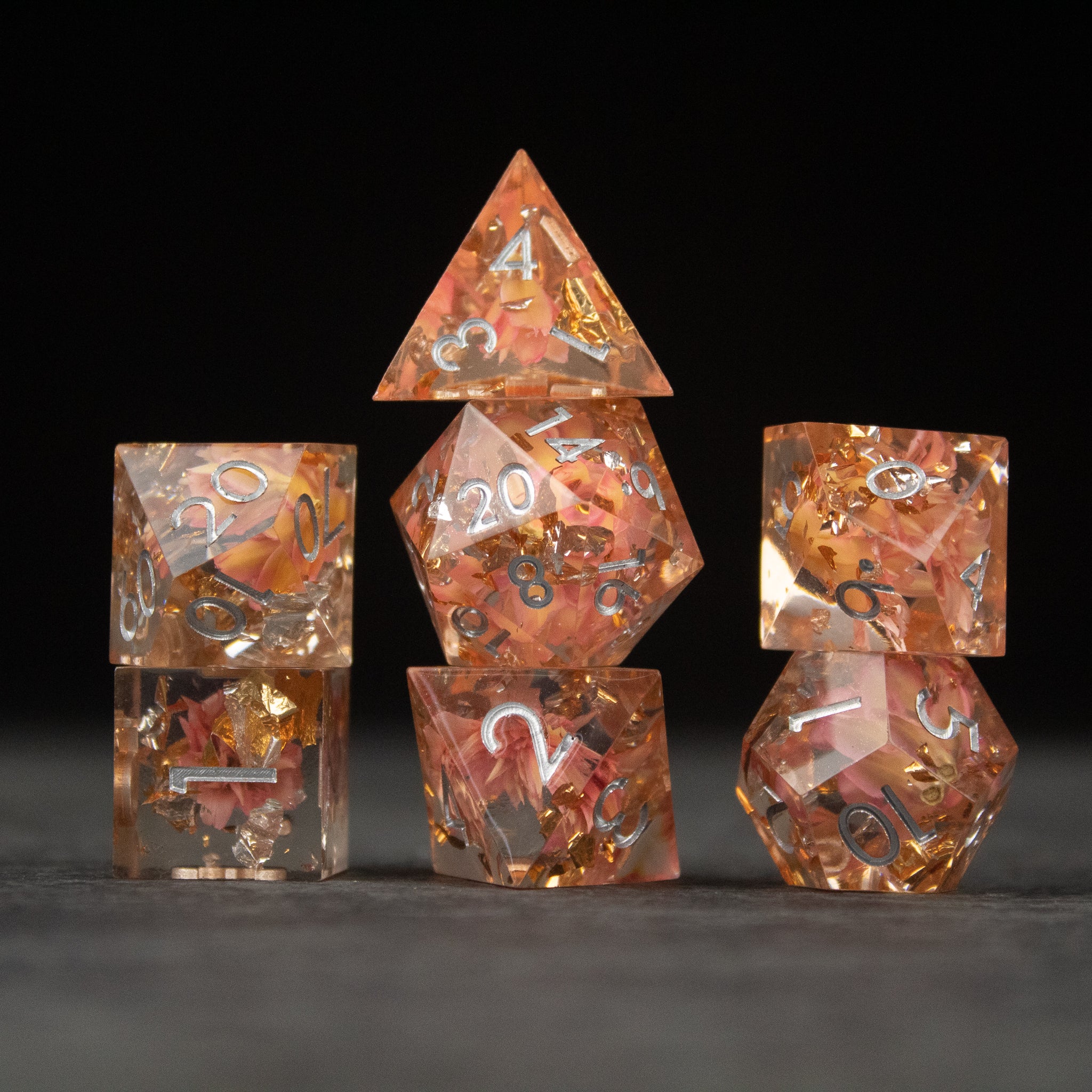 Pink Flower Sharp Edge Dice Set - Clear pink sharp edge dice set with embedded flower petals and gold numbers on a black background.