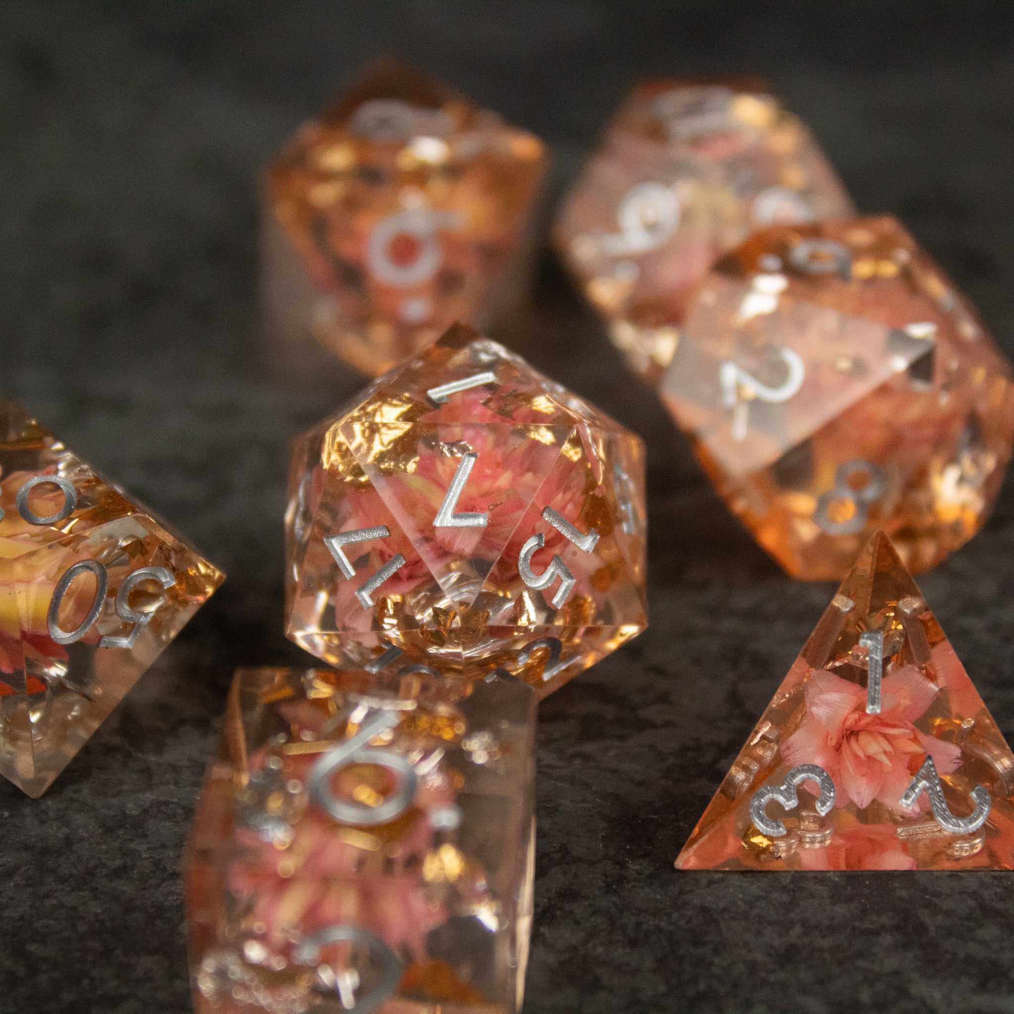 Pink Flower Sharp Edge Dice Set - Translucent pink sharp-edged polyhedral dice with embedded flower petals and white numbering on a dark background.