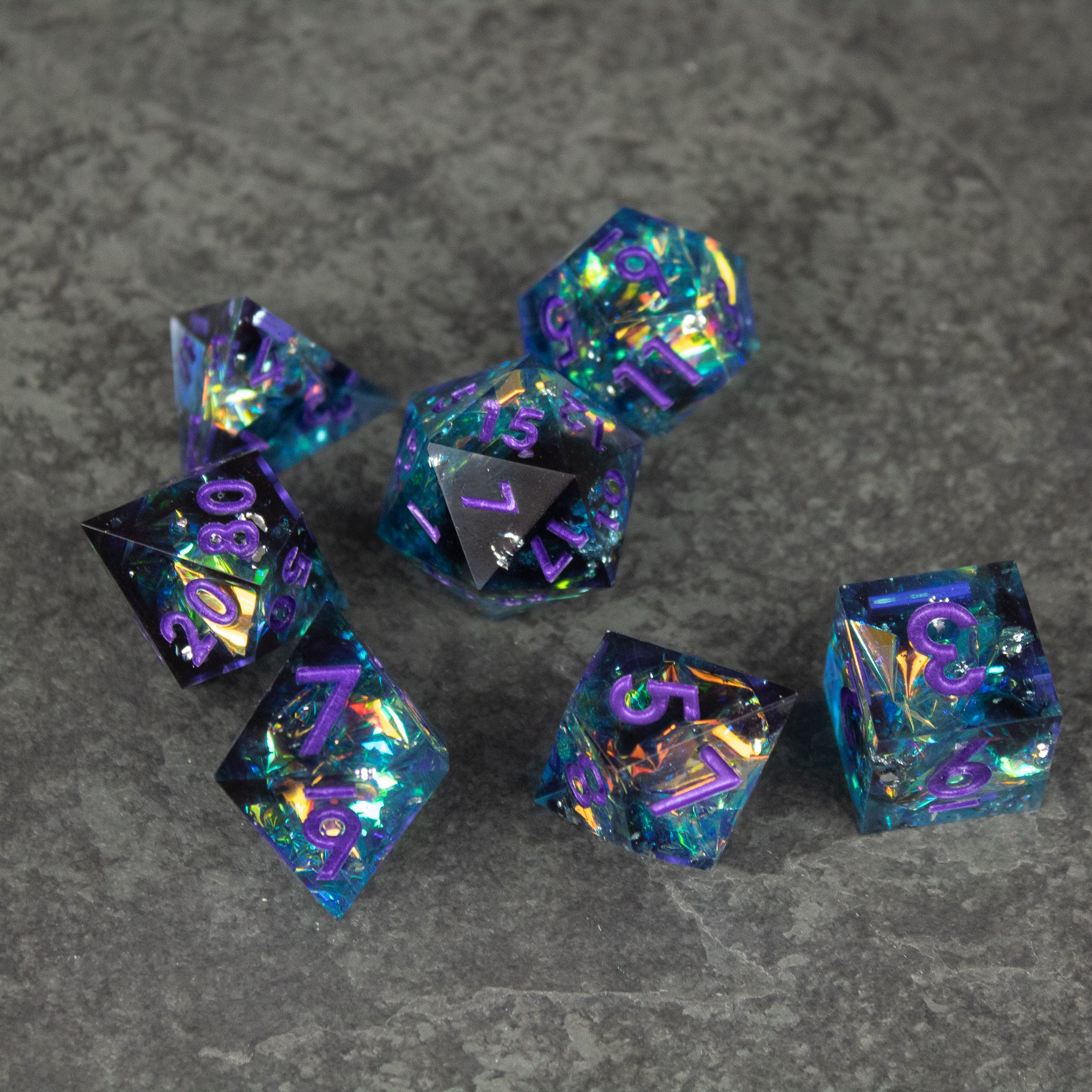 Frostbite Dice Set - Seven translucent blue polyhedral dice with sharp edges and colorful glitter inside on a gray surface.