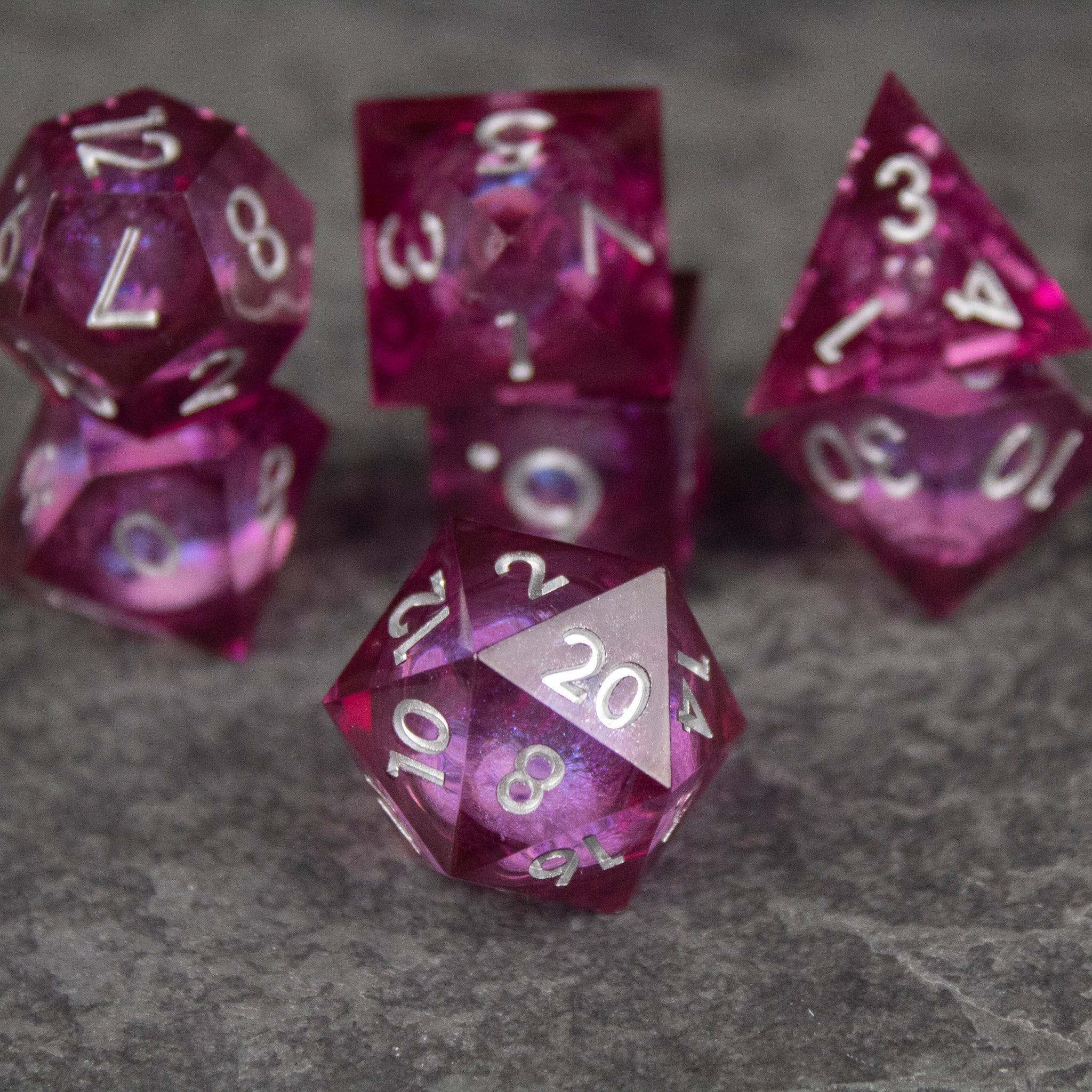 Magic Wine - Liquid Core Dice Set - Set of translucent red sharp-edged polyhedral dice with swirling liquid core and white numbers on gray surface.