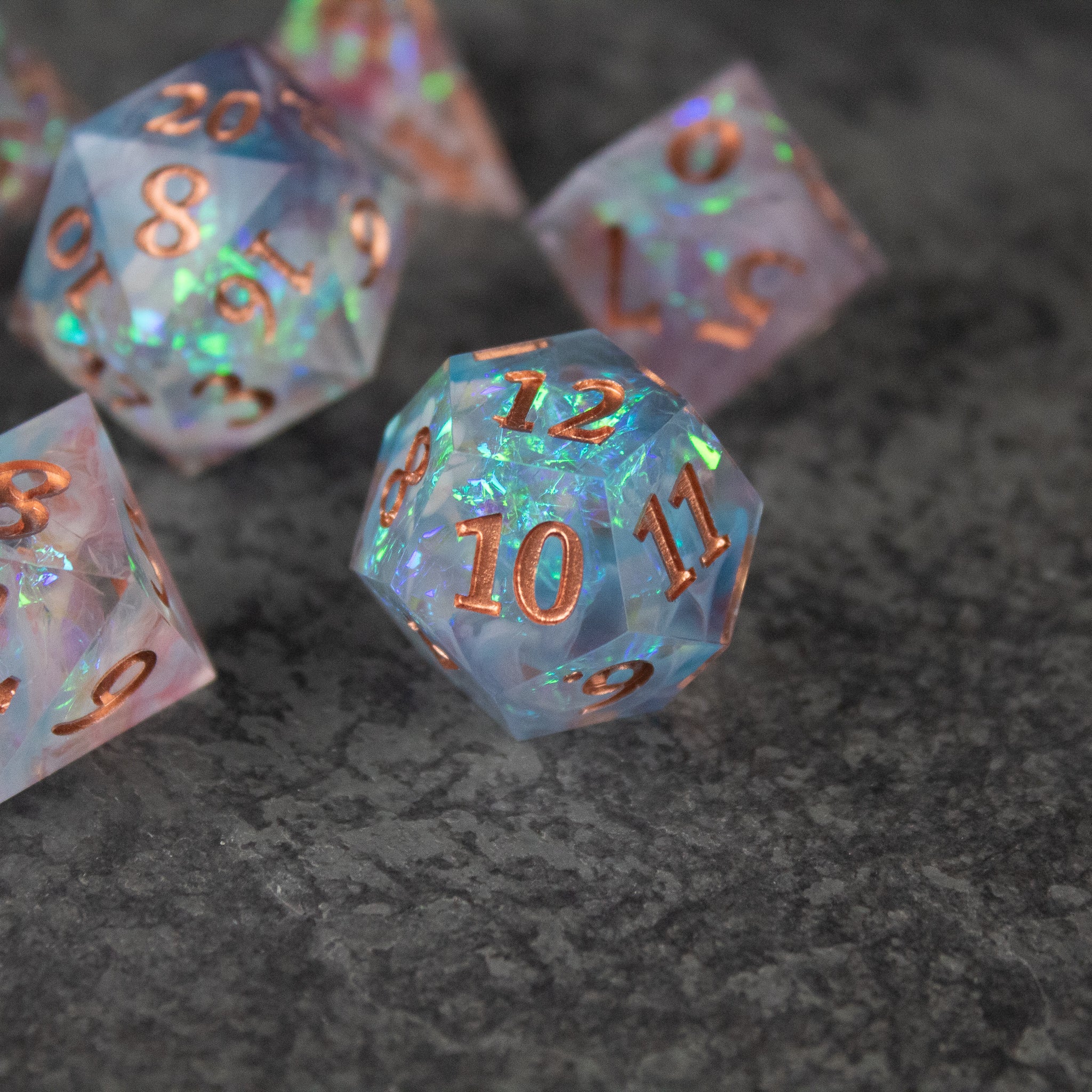 Divination Dice Set - Translucent multi-colored d20 dice with sharp edges and rose gold numbers on dark textured surface.