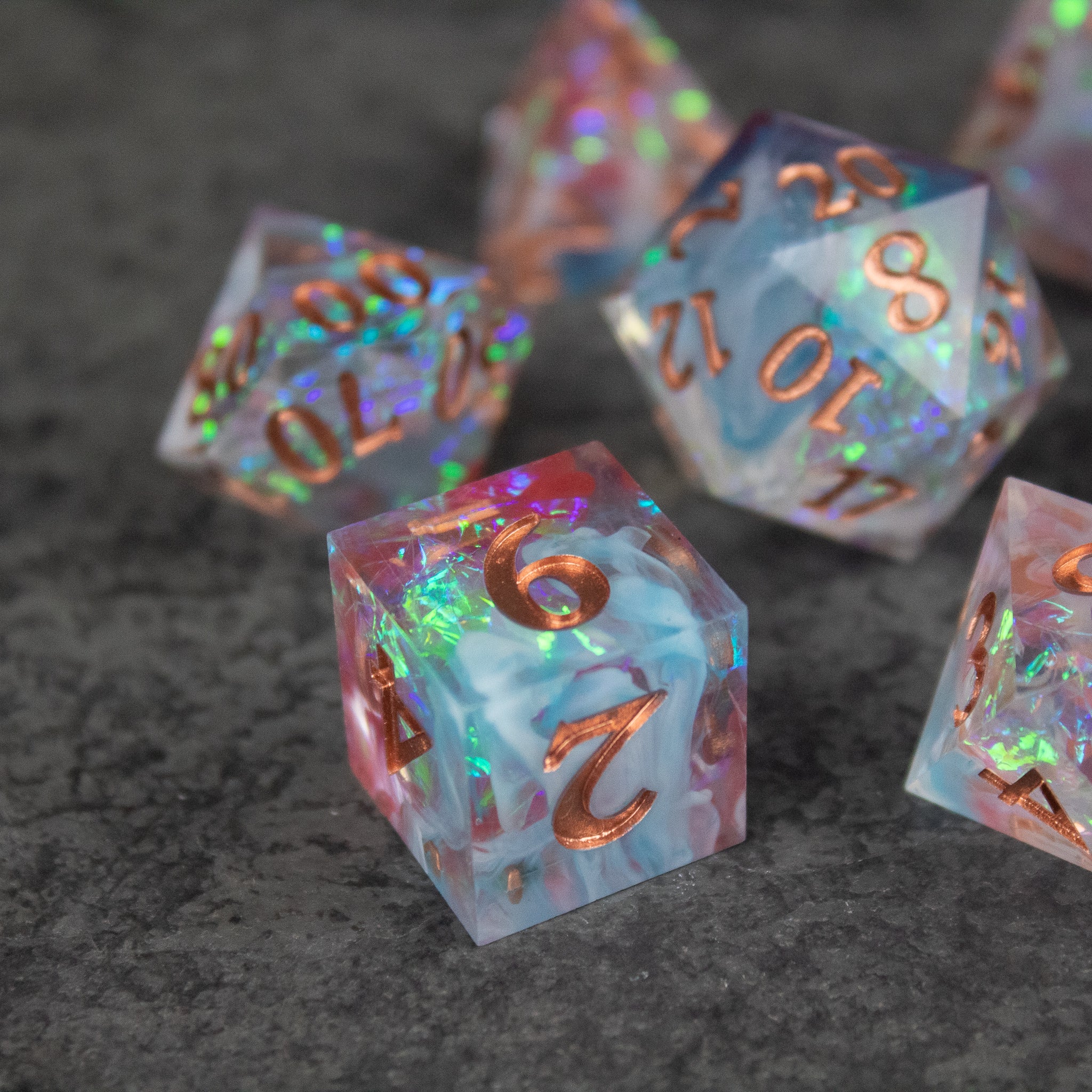 Divination Dice Set - Translucent pink and blue sharp-edged dice with gold and holographic numbers on a dark surface.