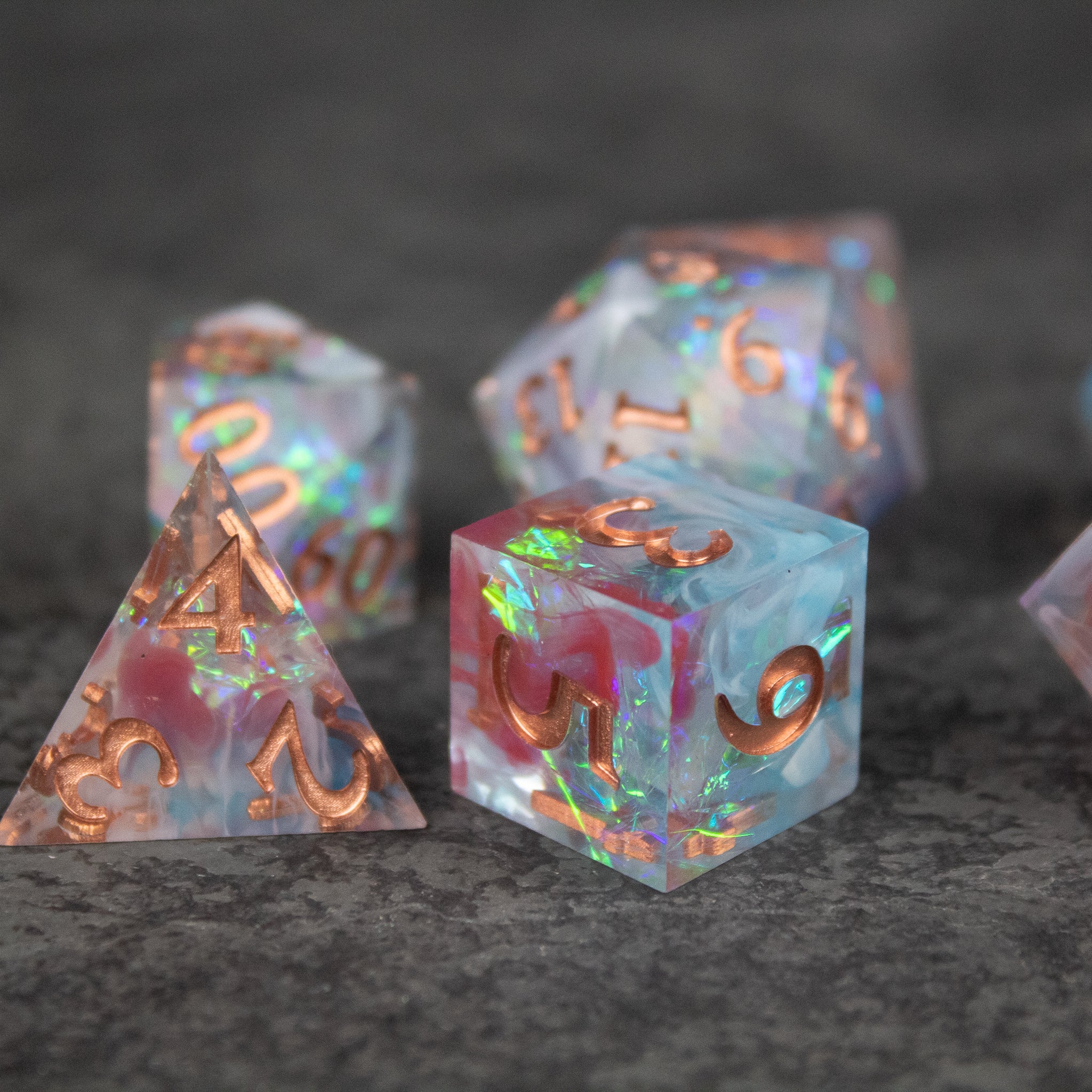 Divination Dice Set - Translucent multicolored sharp-edged polyhedral dice set with metallic gold numbering on gray surface.