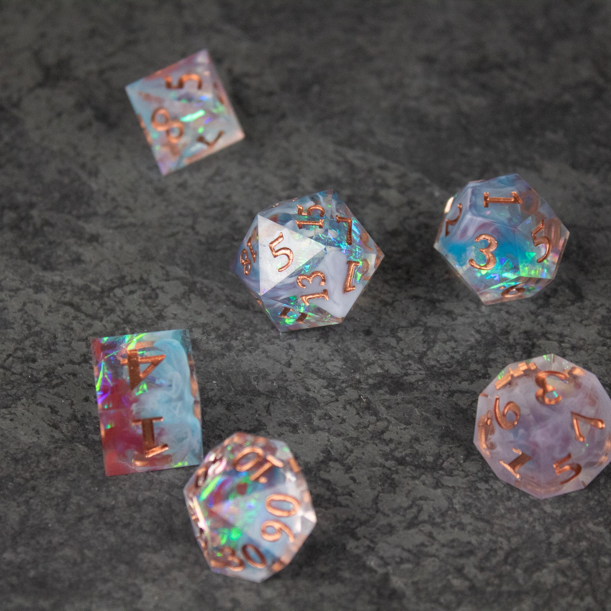 Divination Dice Set - Set of six translucent polyhedral dice with sharp edges and numbers in metallic rose gold on swirled blue, pink, and purple.