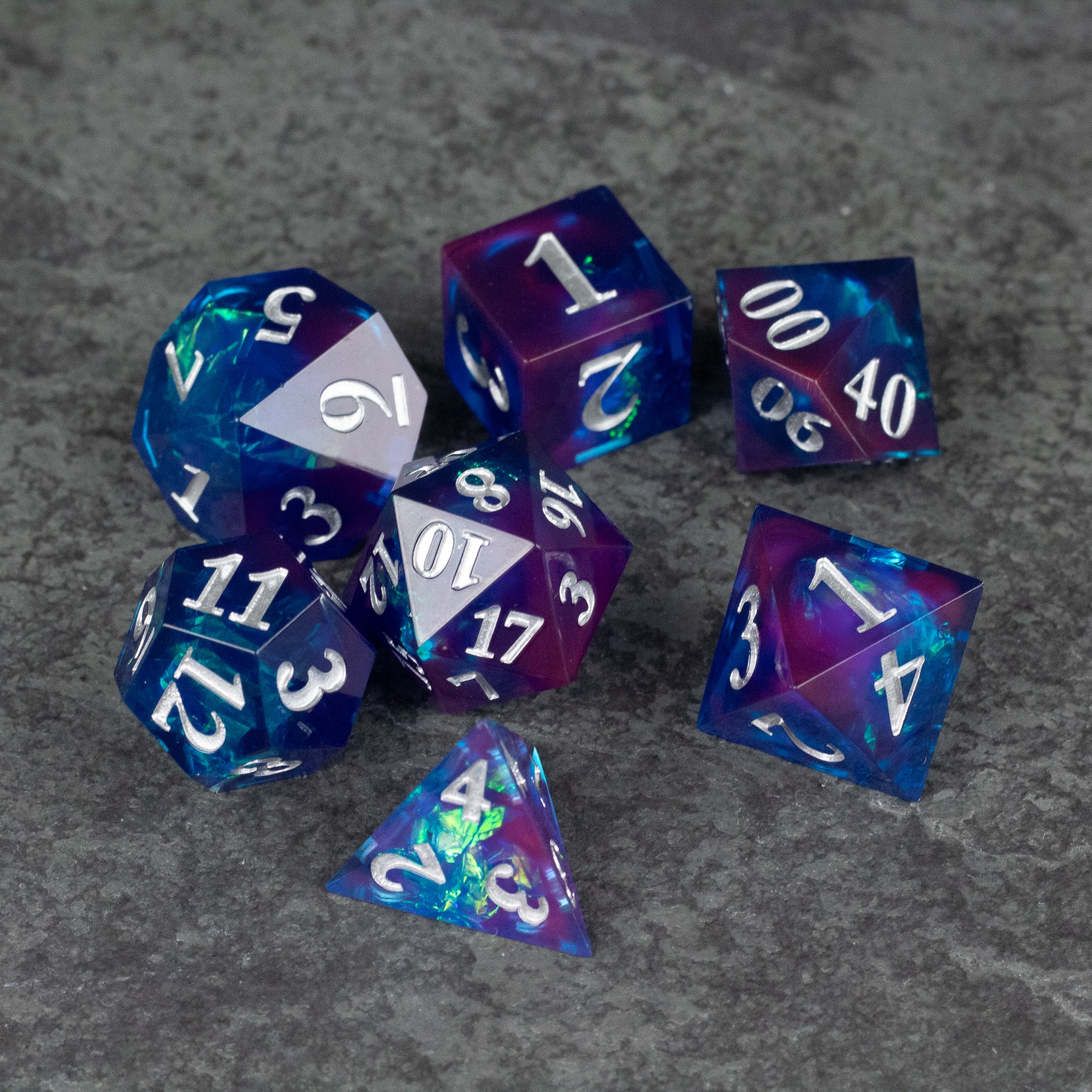 Midnight Blue Dice Set - Set of seven sharp-edged, translucent midnight blue polyhedral dice with white numbers on gray surface.