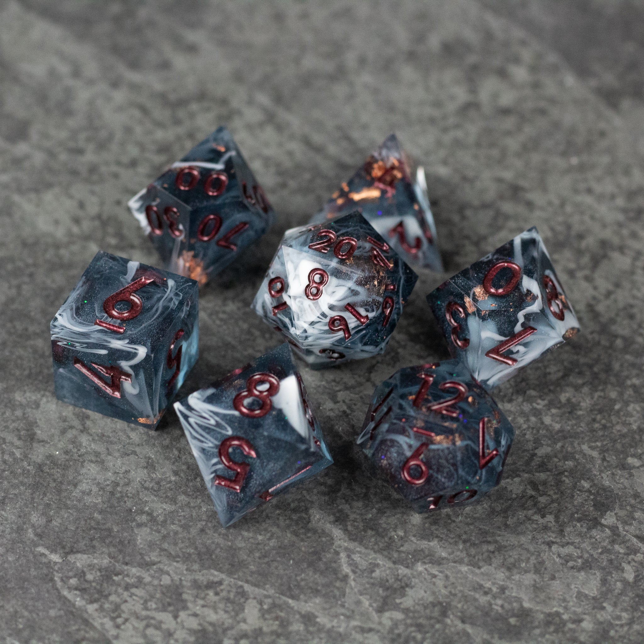 Omen Dice Set - Black sharp-edged dice set with red numbering and smoky marbled design on gray stone surface.