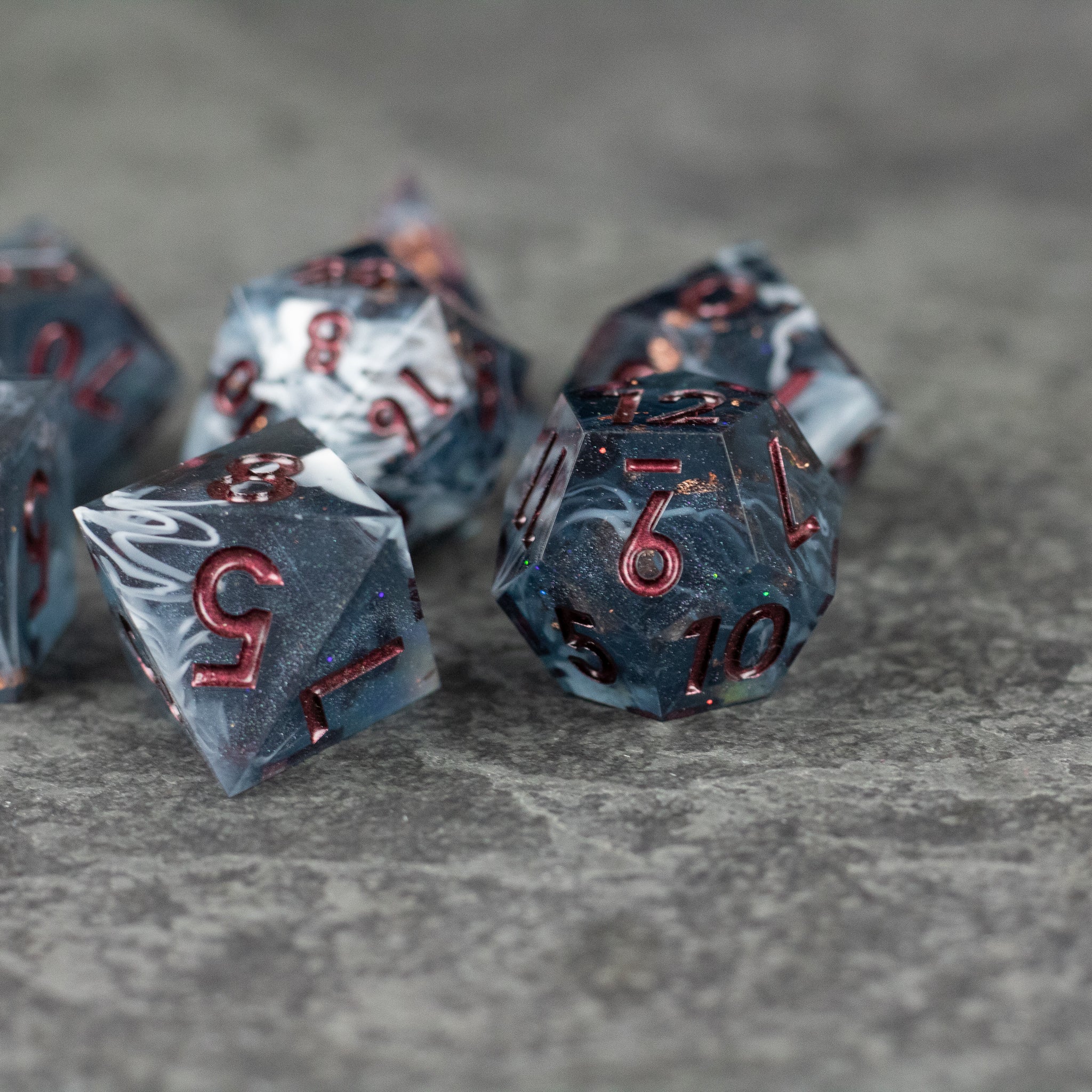 Omen Dice Set - Black and gray marbled sharp-edged polyhedral dice with red numbers on a gray surface.