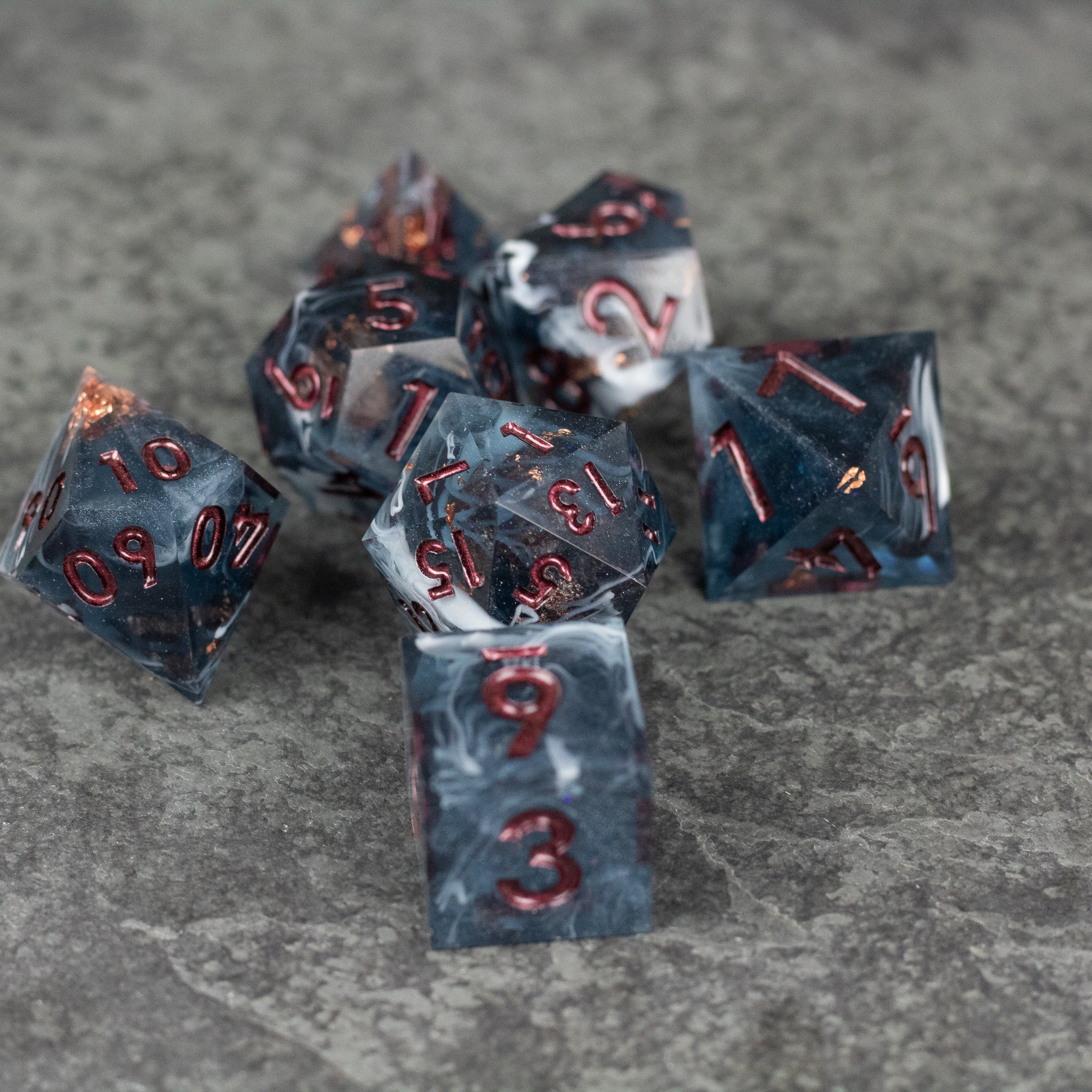 Omen Dice Set - Set of seven black and gray marbled sharp-edged dice with red numbers on gray stone surface.