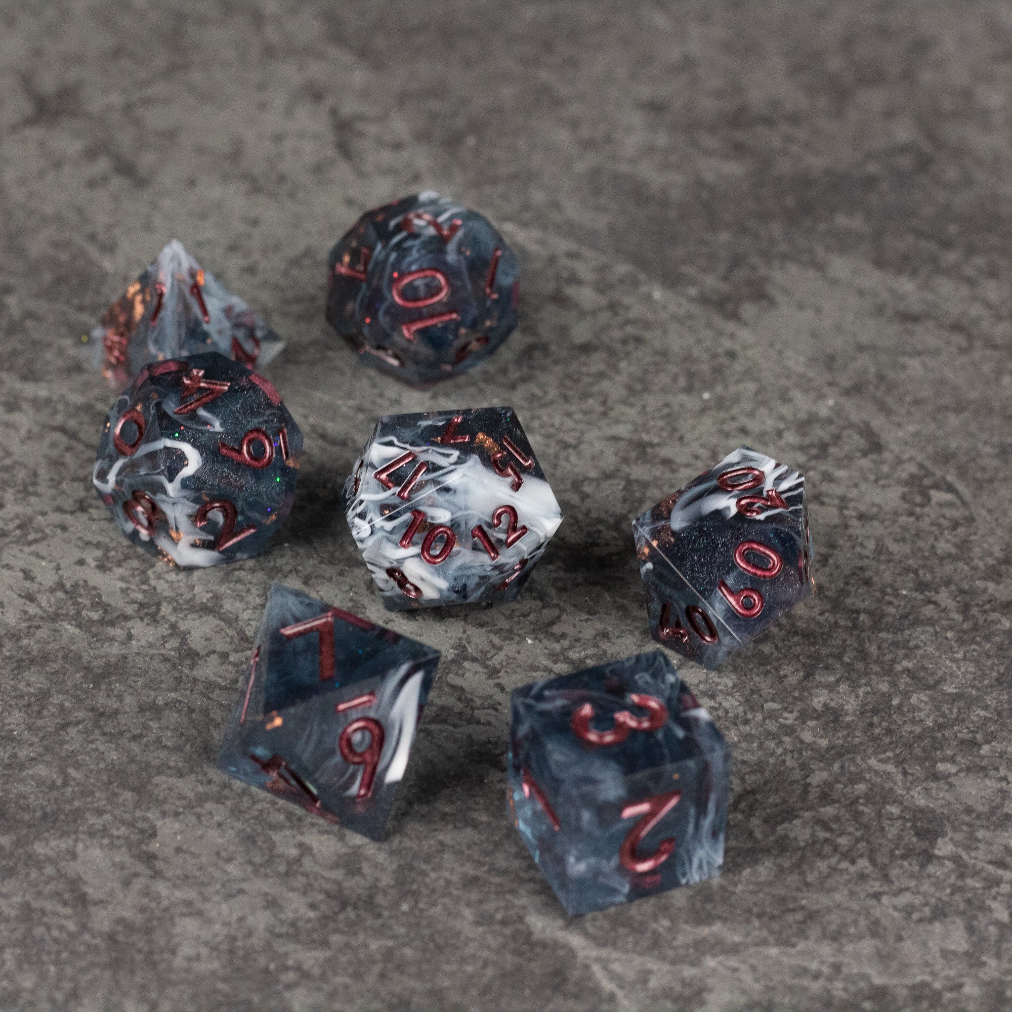 Omen Dice Set - Black and gray marbled sharp-edged dice set with red numbering on a textured gray surface.