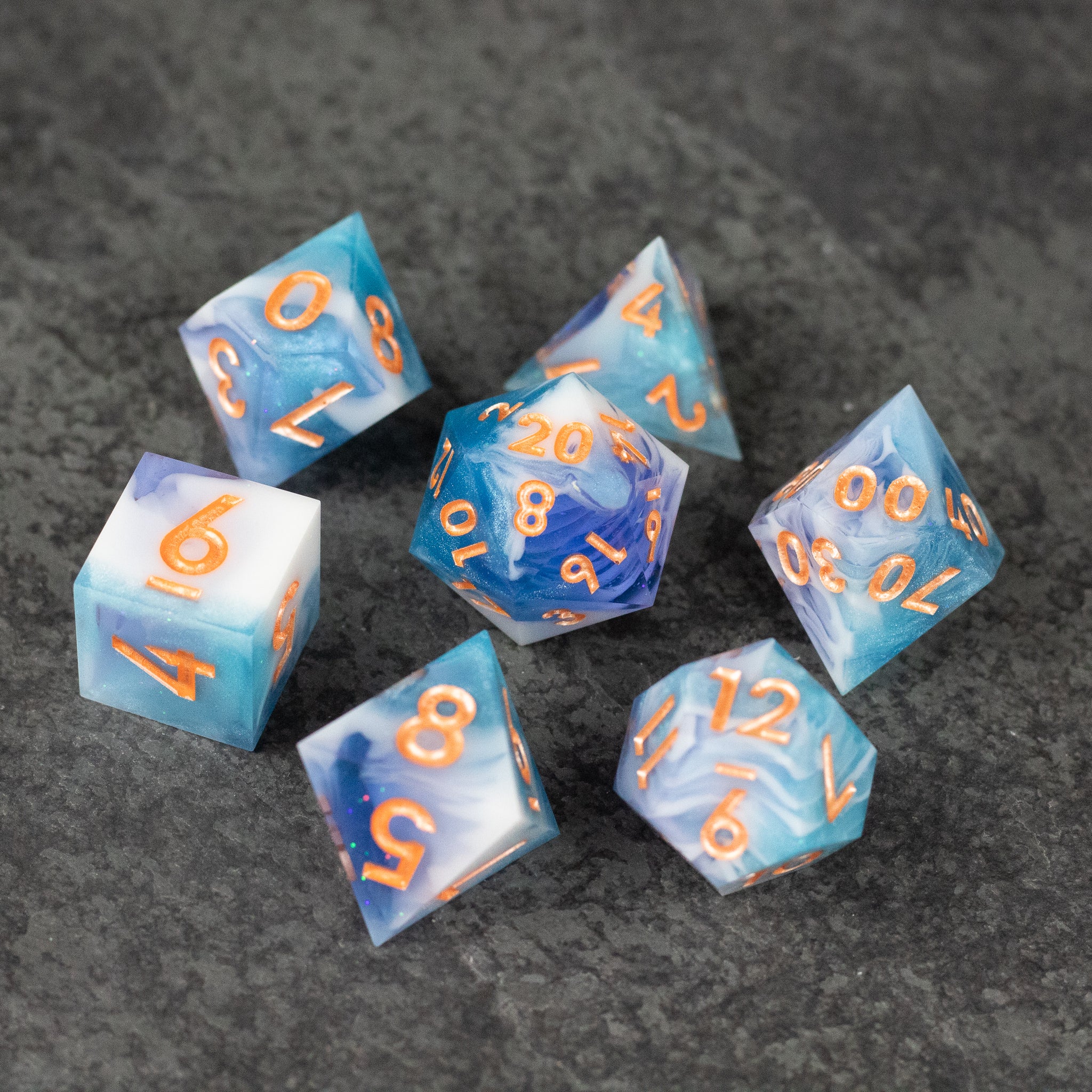 Cloudscape Dice Set - Blue and white sharp-edged polyhedral dice set with orange numbers on a gray surface.