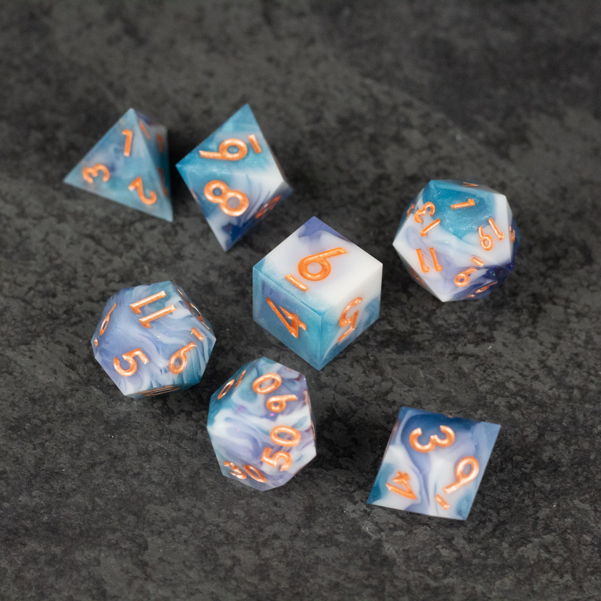 Cloudscape Dice Set - Seven blue sharp-edged polyhedral dice with white cloud patterns and orange numbers on a dark surface.