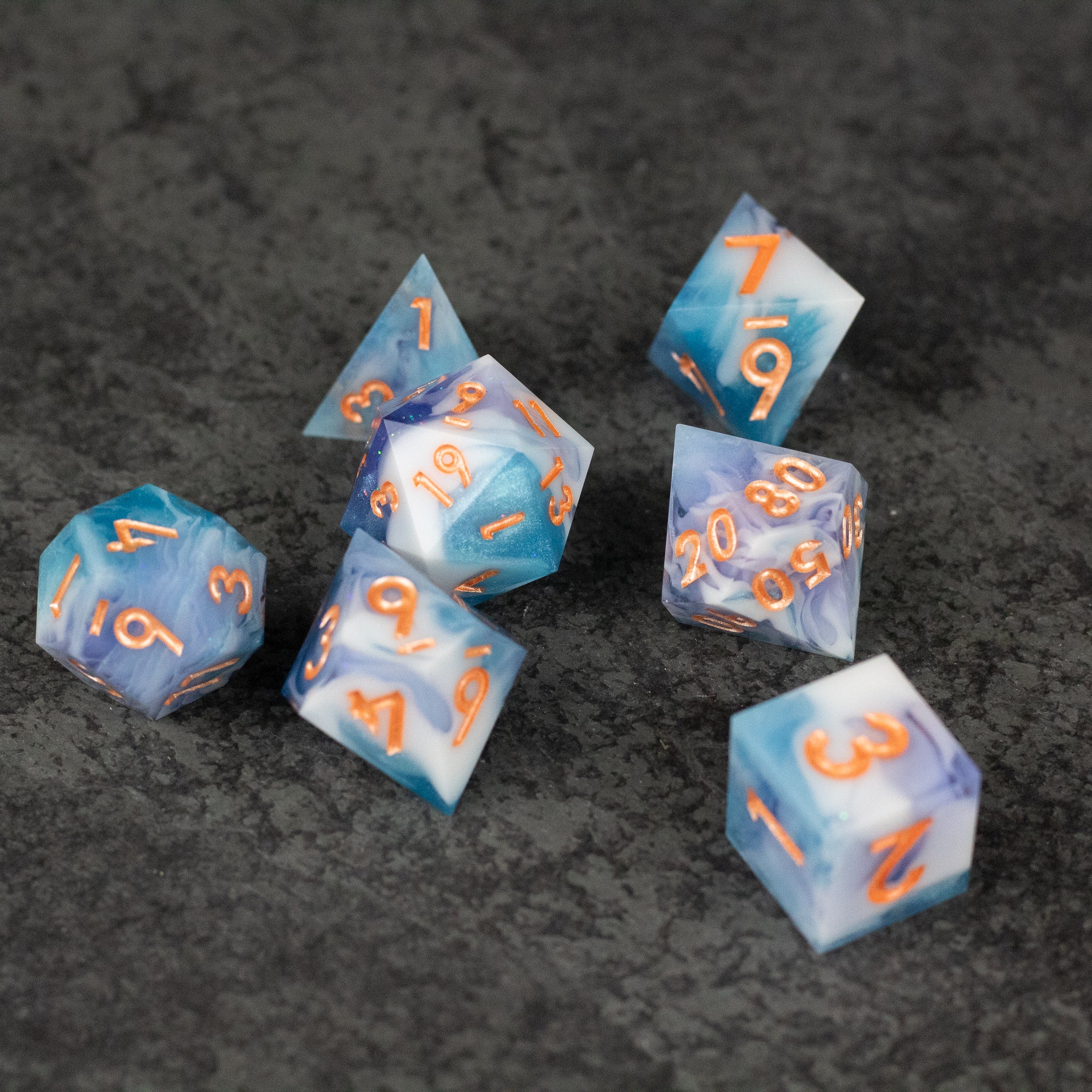 Cloudscape Dice Set - Set of seven sharp-edged dice with white and blue cloud-like patterns and orange numbers.