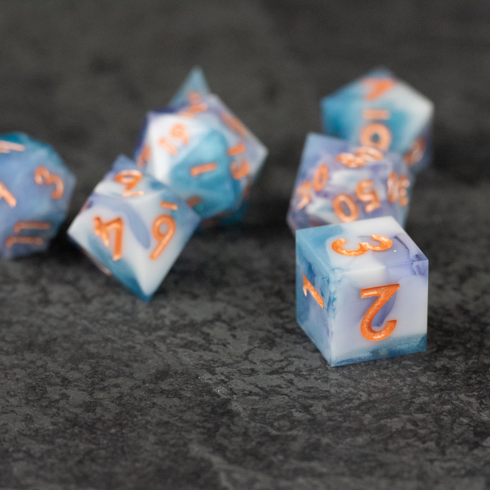 Cloudscape Dice Set - Set of blue and white sharp-edged dice with orange numbers on a dark textured surface.