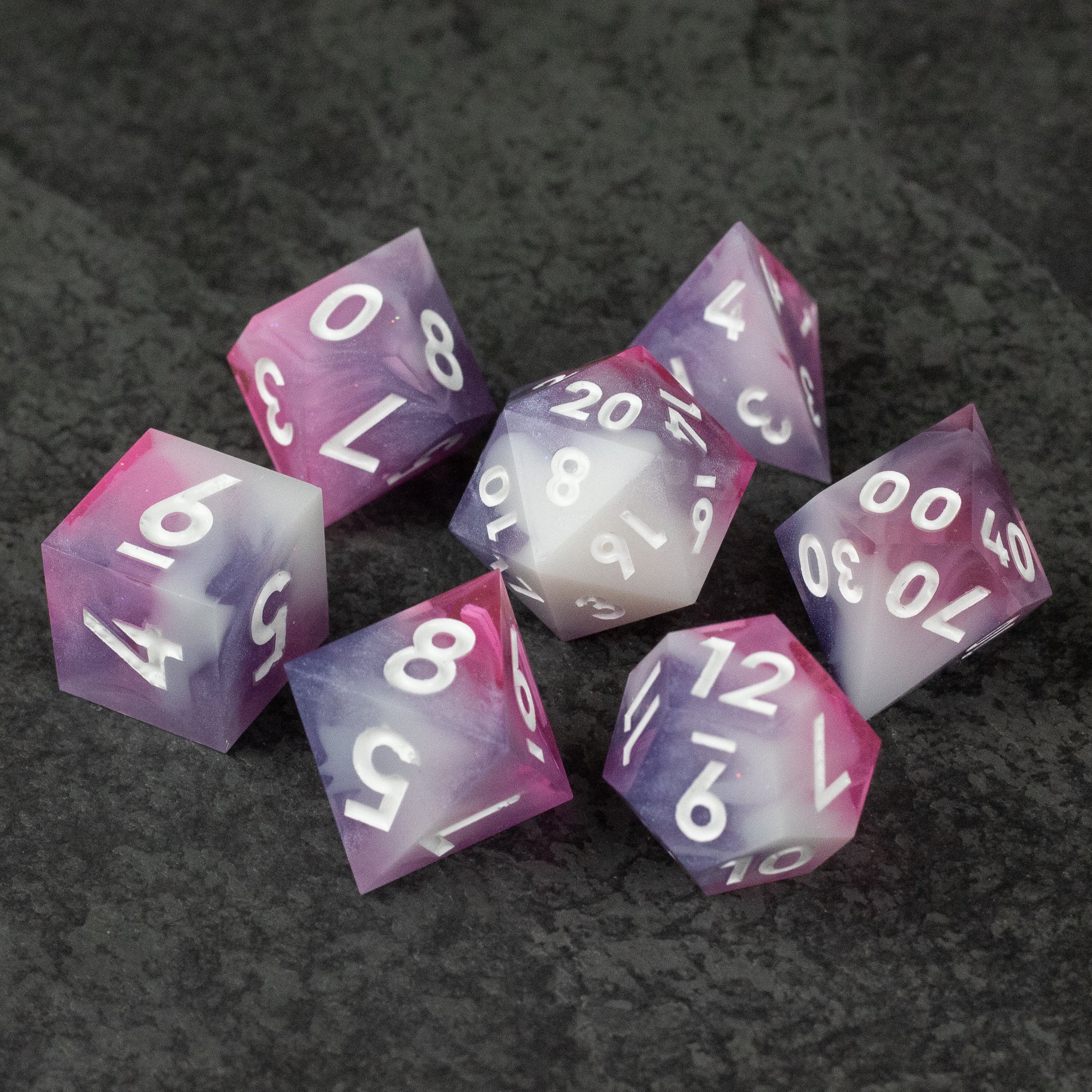 Melody Dice Set - Set of seven sharp-edged dice in pink and purple hues with white numbers on a dark textured surface.