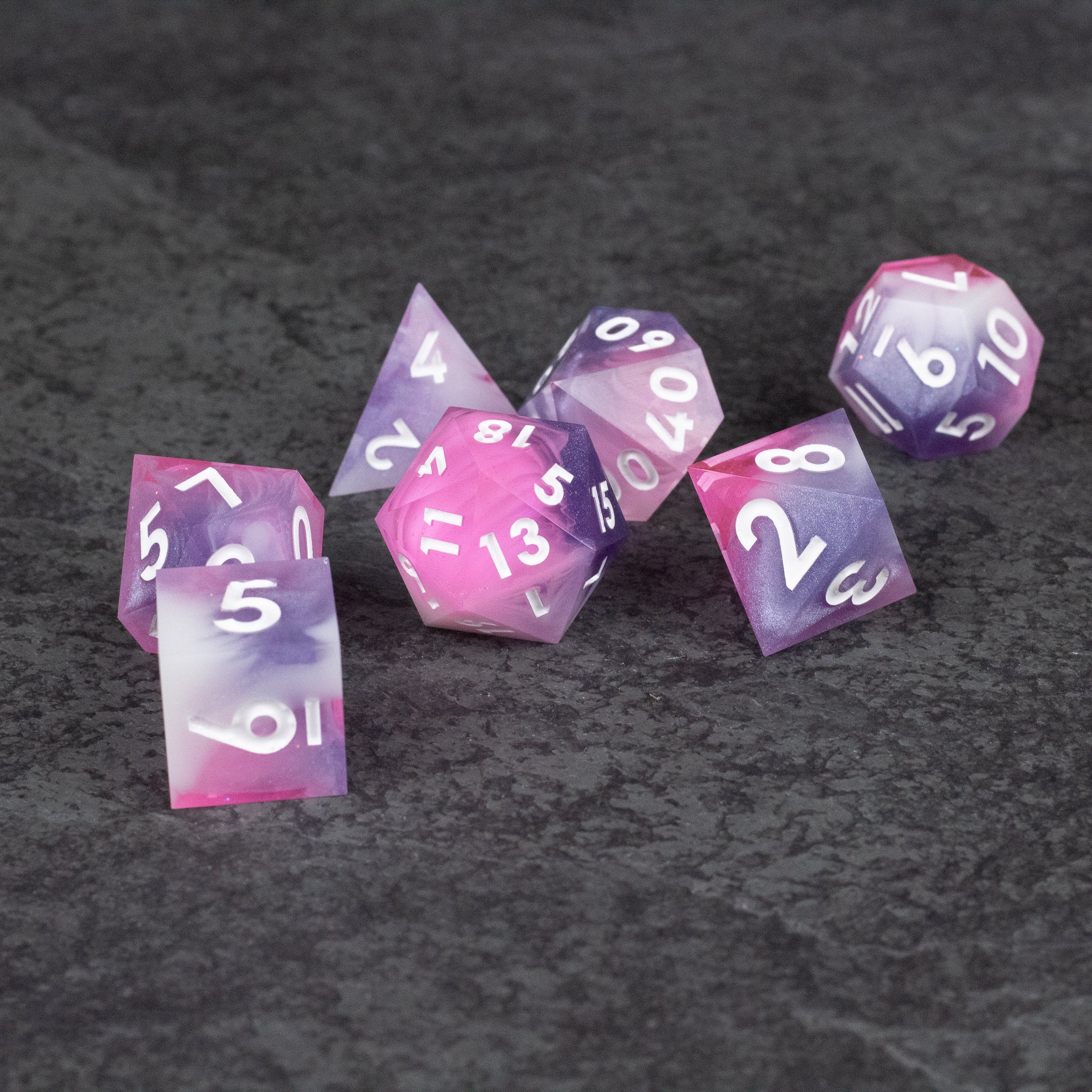 Melody Dice Set - Set of seven sharp-edged dice in translucent pink and purple with white numbers on dark gray surface.