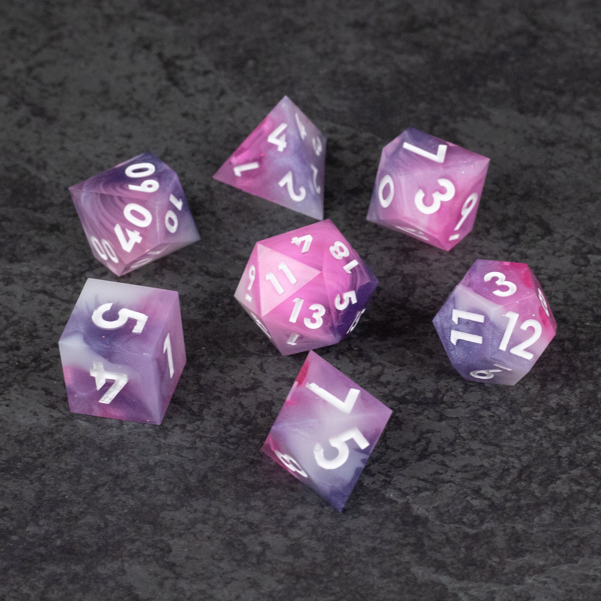 Melody Dice Set - Set of seven sharp-edged polyhedral dice in varying shades of pink with white numbers on a dark textured surface.