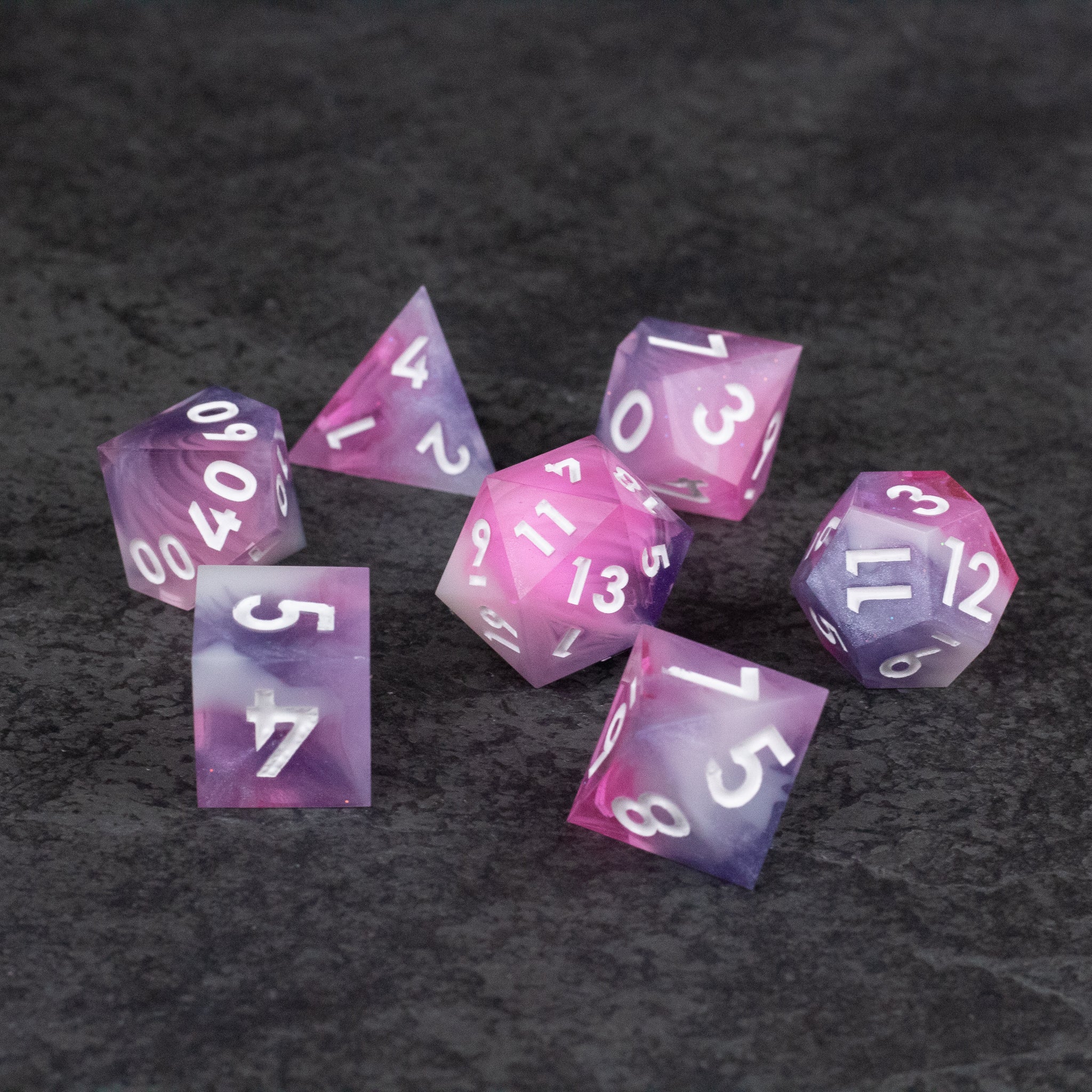 Melody Dice Set - Seven pink and white marbled sharp-edged polyhedral dice with white numbers on a dark textured surface.