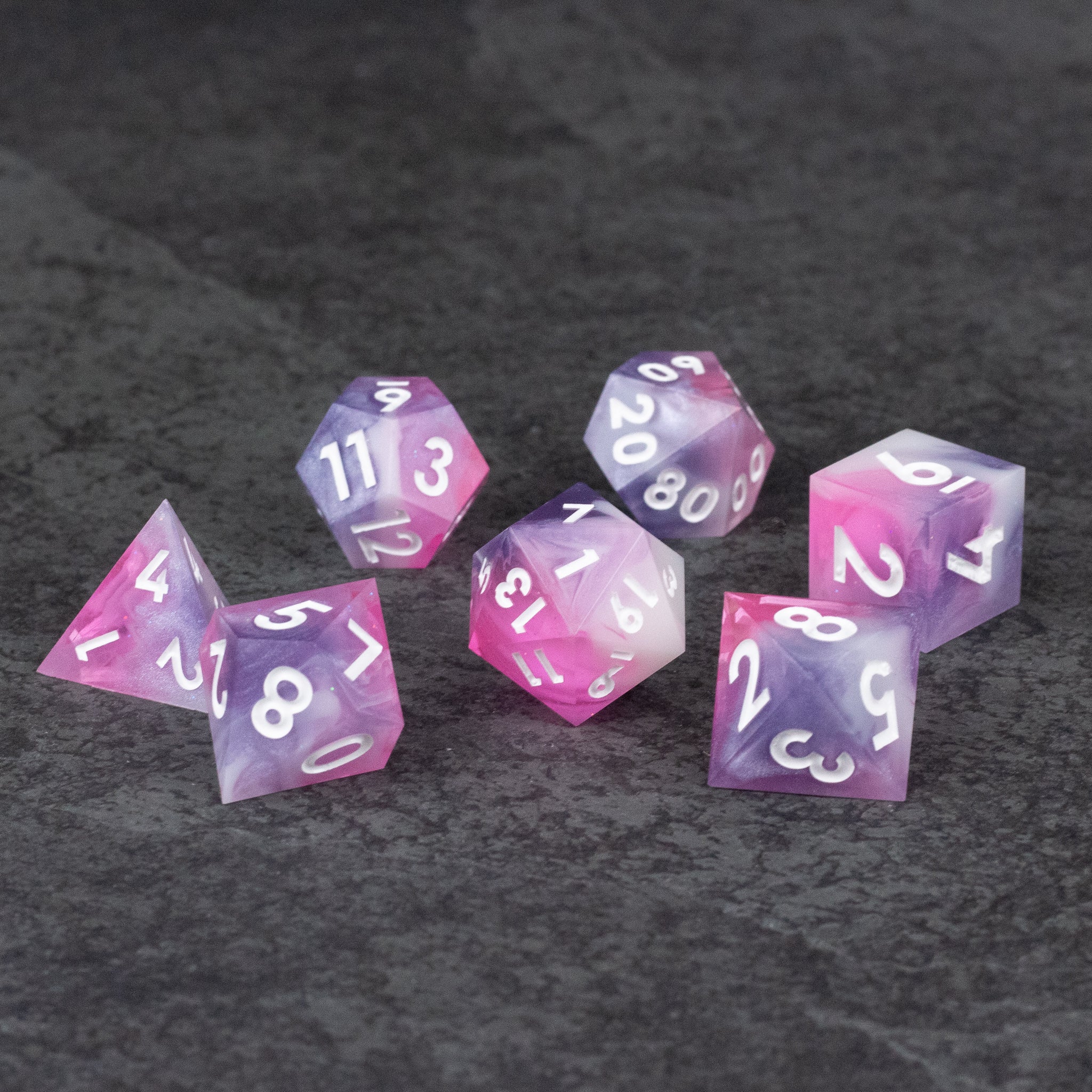 Melody Dice Set - Set of seven sharp-edged translucent pink polyhedral dice with white numbers on dark gray background.