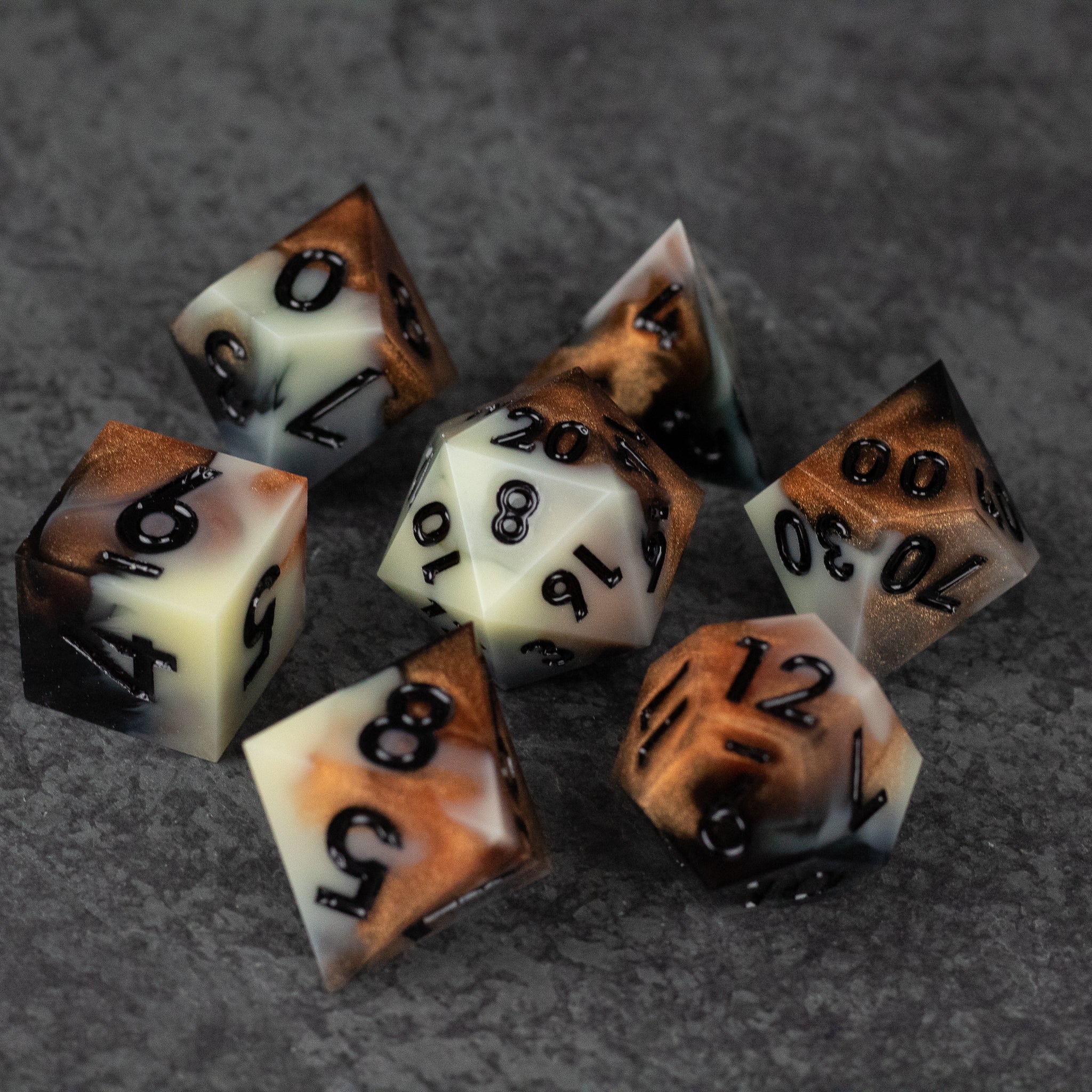 Dwarven Delight Dice Set - Seven sharp-edged polyhedral dice in black, white, and bronze with clear numbering on granite surface.