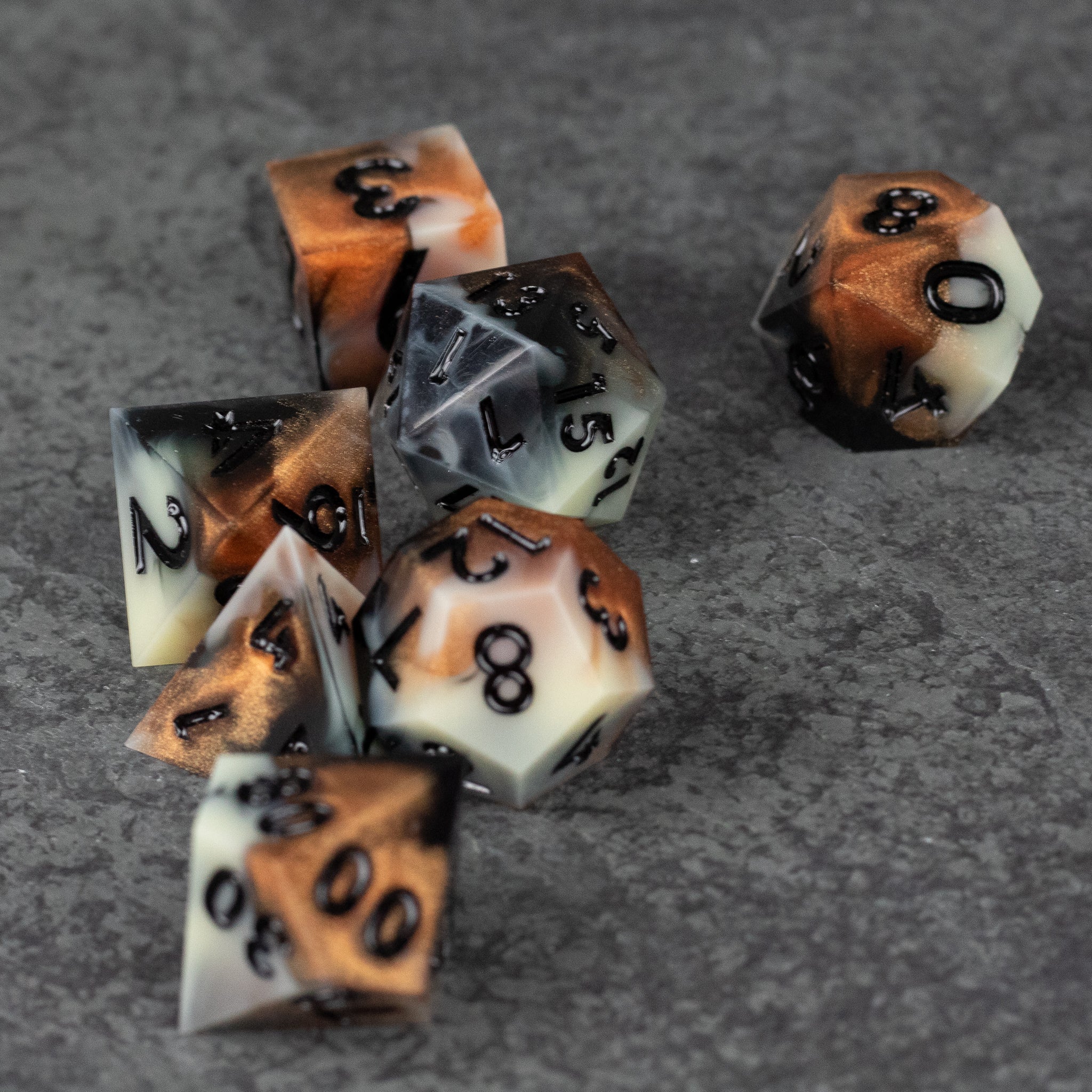 Dwarven Delight Dice Set - Set of seven sharp-edged polyhedral dice in black, copper, and white marbled resin with black numbers.