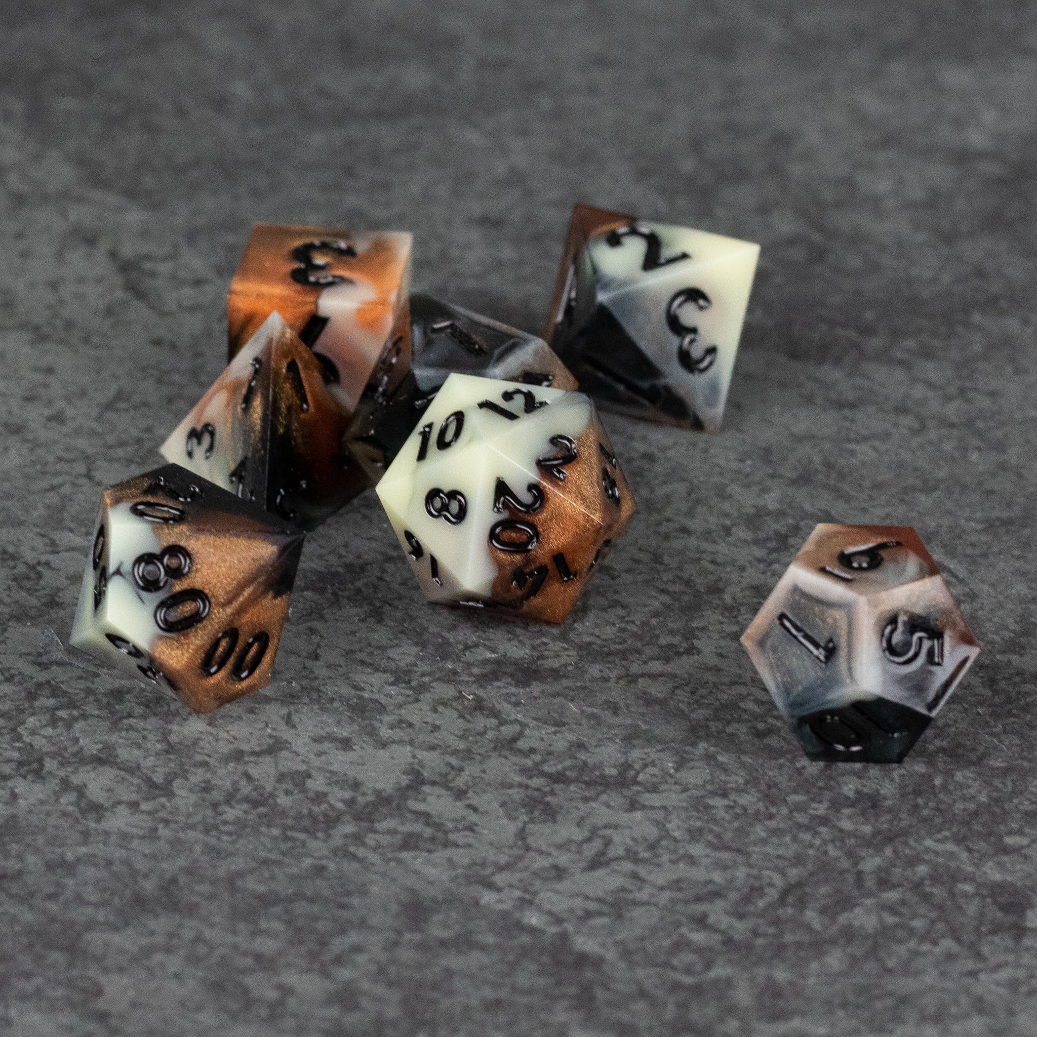 Dwarven Delight Dice Set - Seven sharp-edged polyhedral dice with black numbers in white, brown, and gray marbled colors on a gray textured surface.