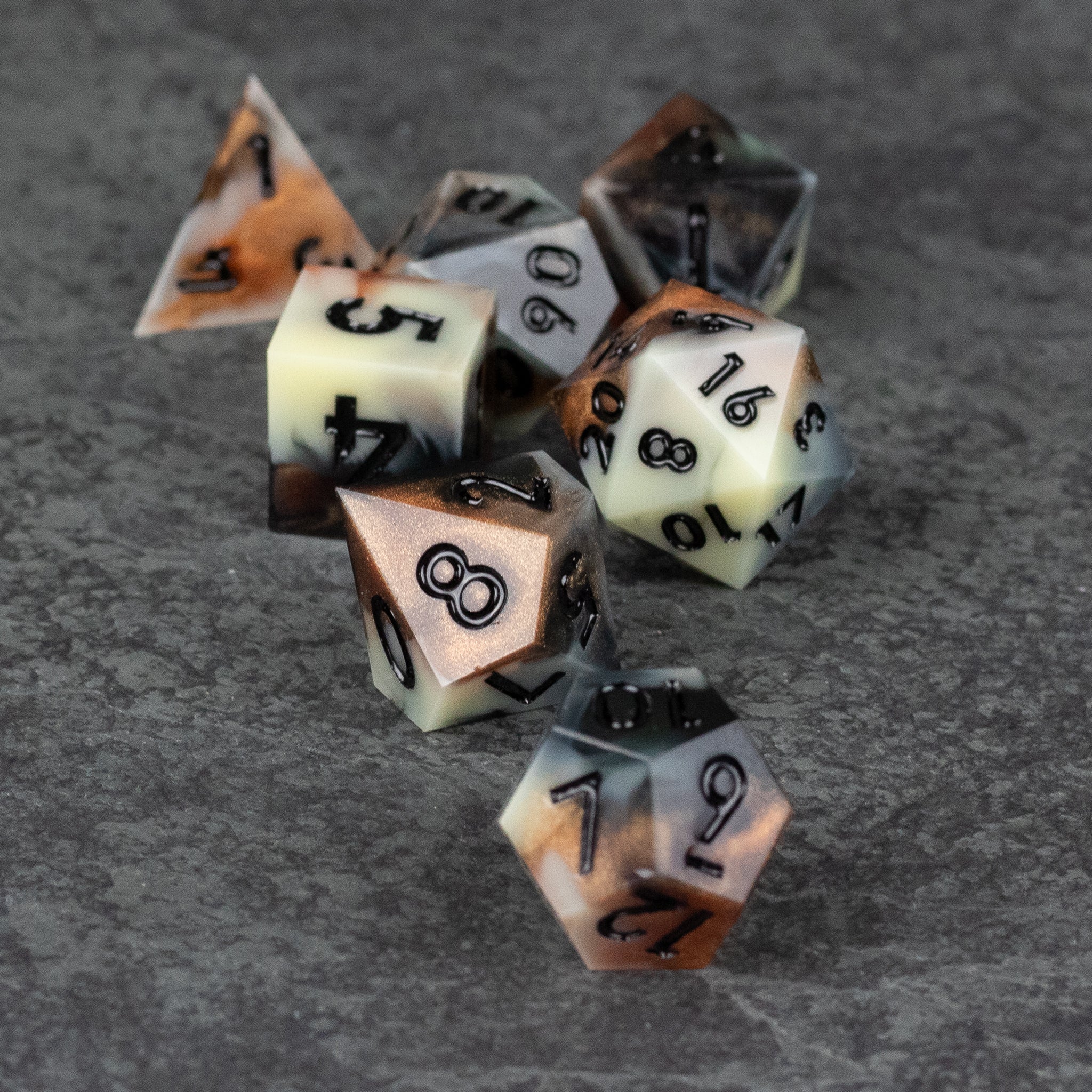 Dwarven Delight Dice Set - Seven polyhedral dice in muted beige, black, and brown with sharp edges and black numbers on a gray textured surface.