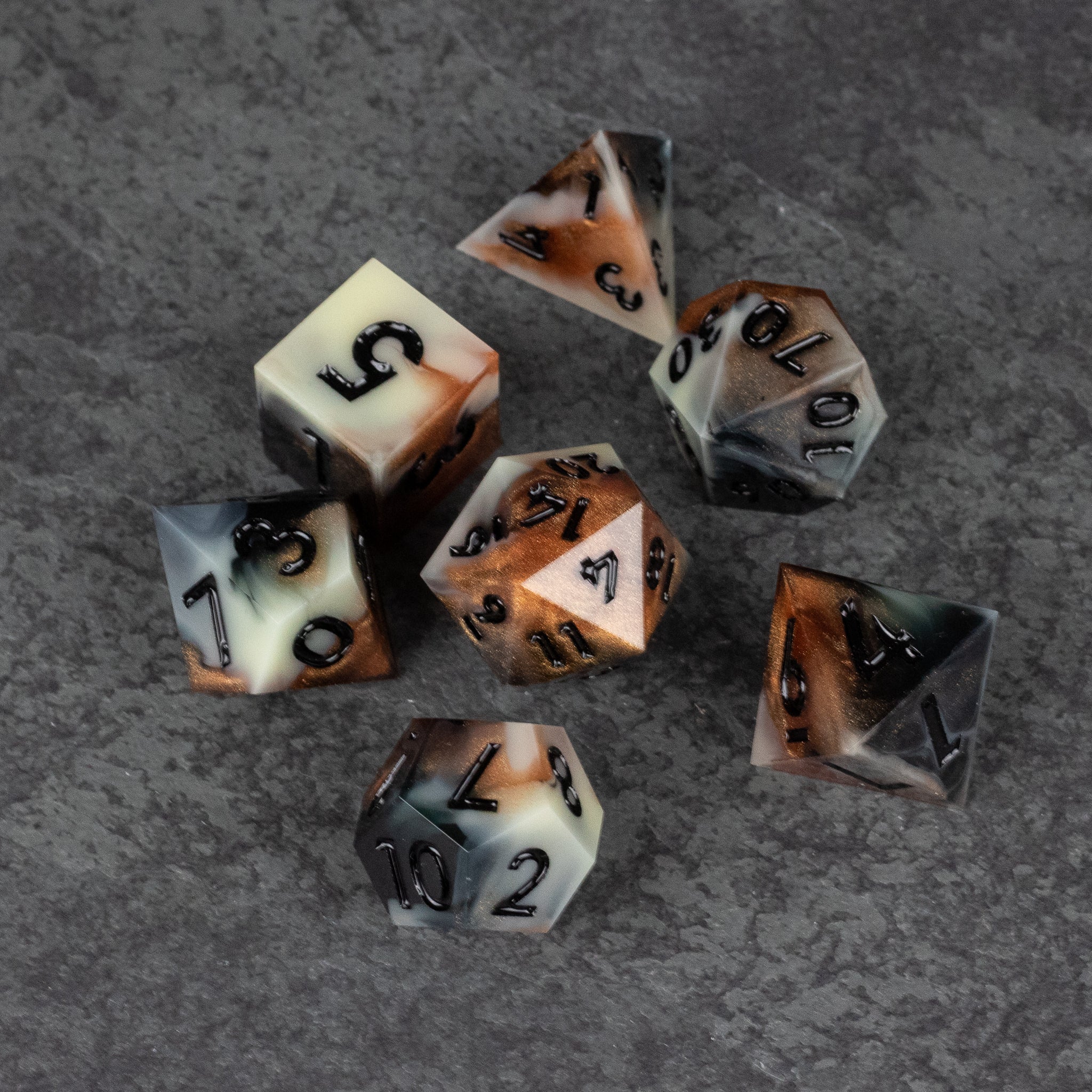 Dwarven Delight Dice Set - Seven sharp-edged polyhedral dice in white and amber gradient with black numbers on a textured gray surface.