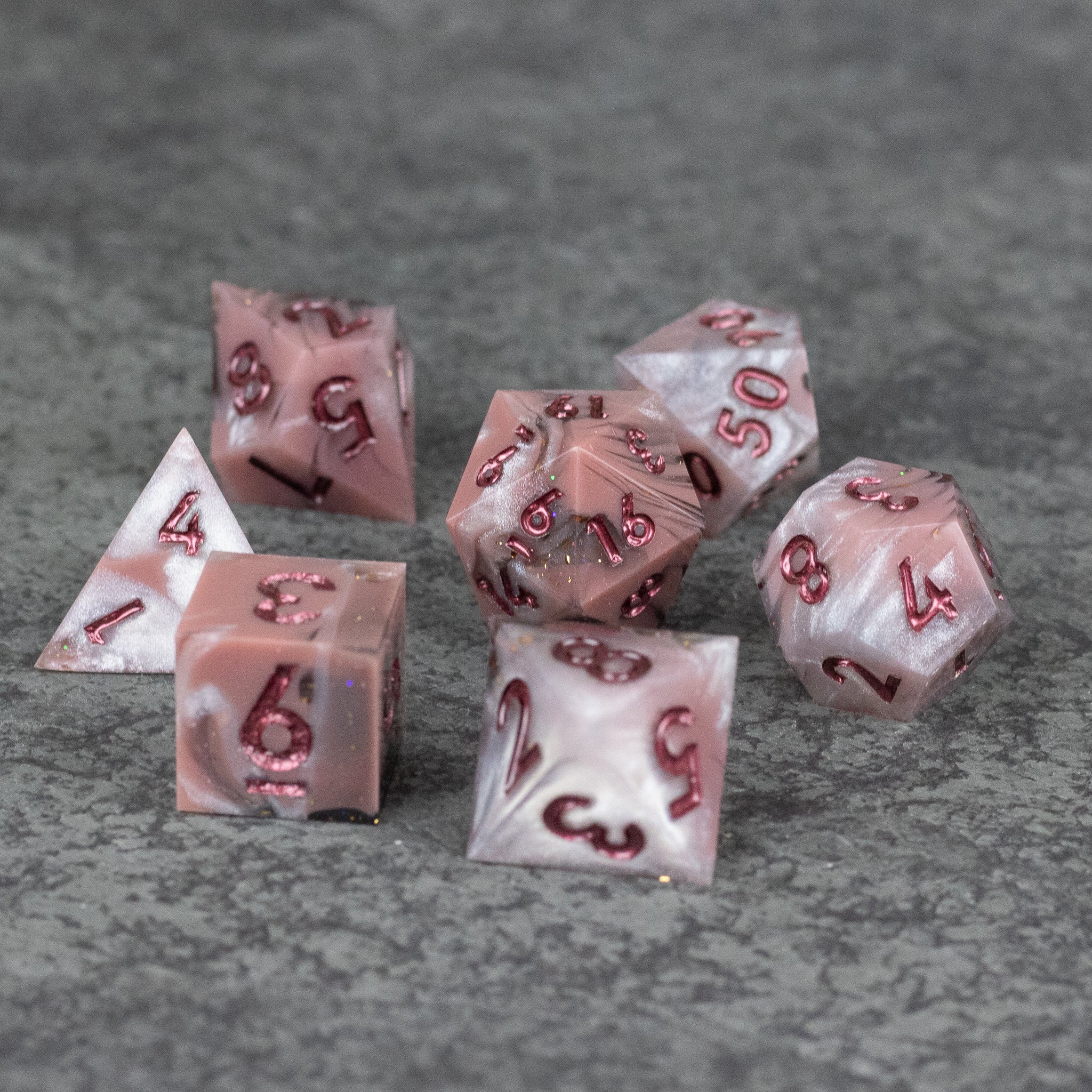 Rosestone Dice Set - Set of seven red and white marbled sharp-edged polyhedral dice with burgundy numbers on gray surface.