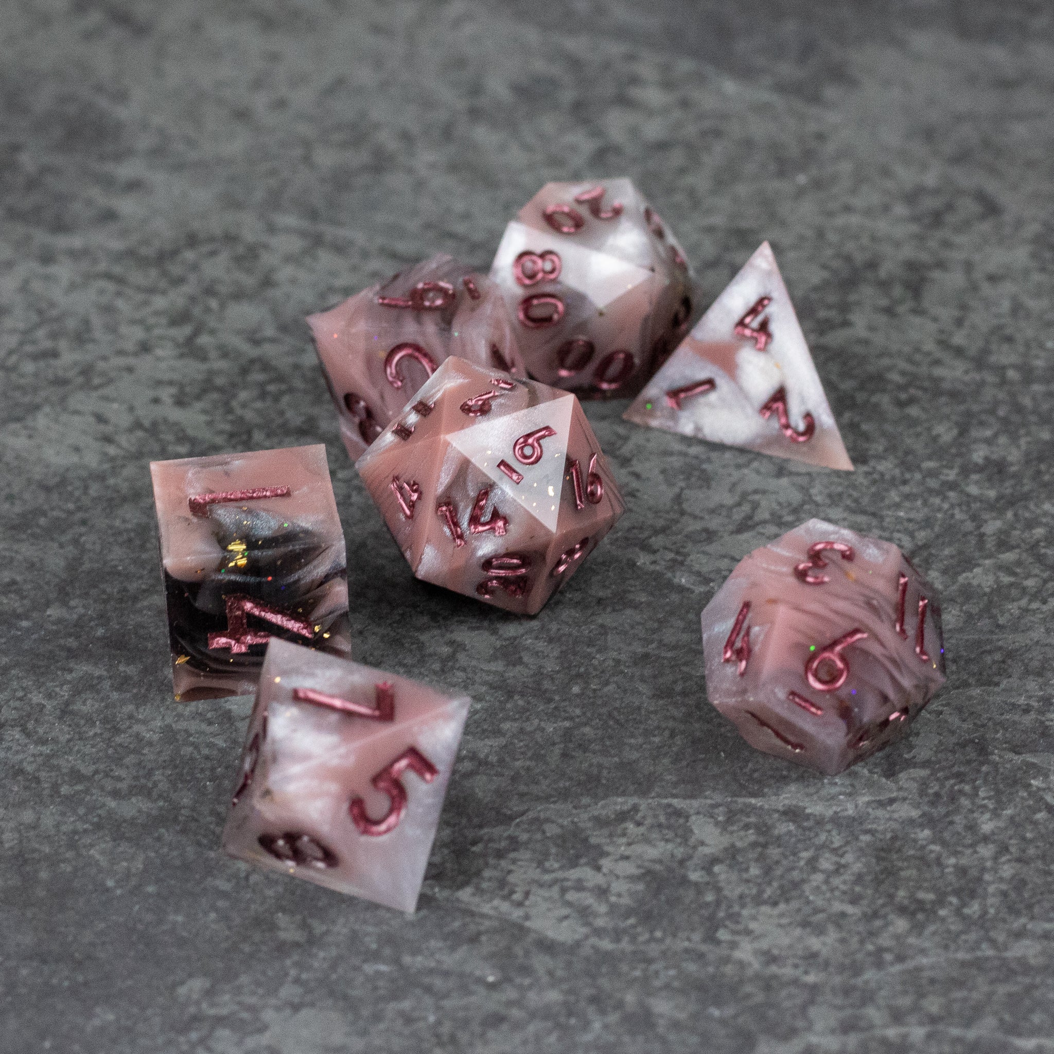 Rosestone Dice Set - Seven-piece set of translucent red and white sharp edge polyhedral dice on gray surface.